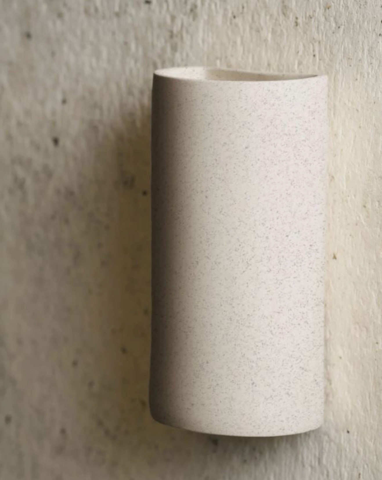 Cylindrical ceramic sconce on a textured beige background