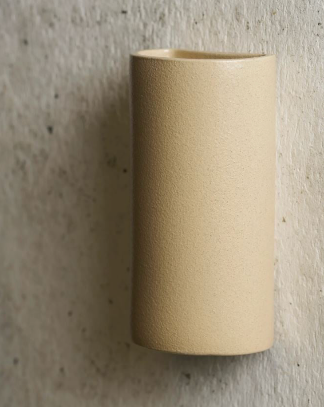 Beige cylindrical ceramic sconce on a textured grey background