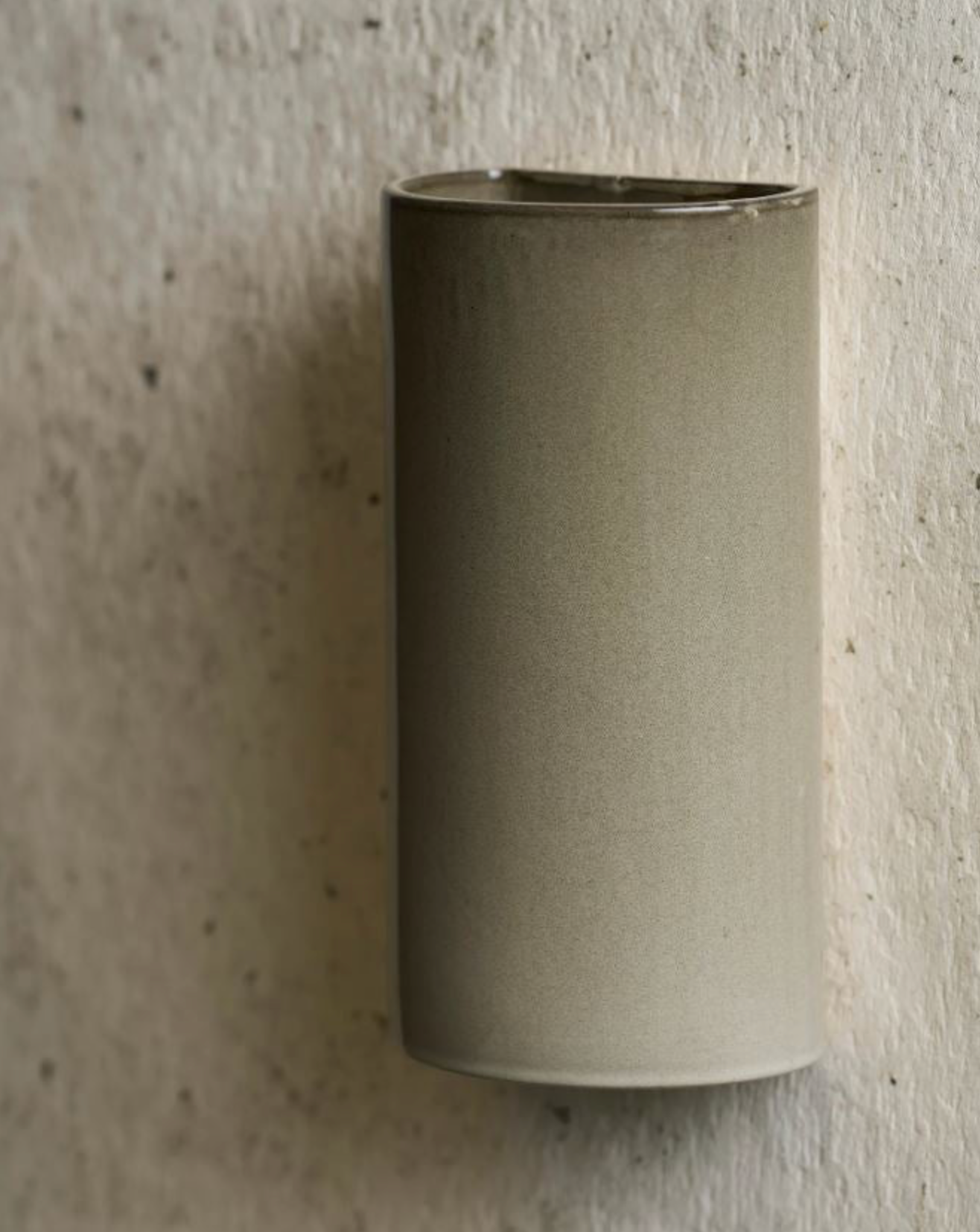 Cylindrical ceramic wall-mounted light fixture on a textured wall.