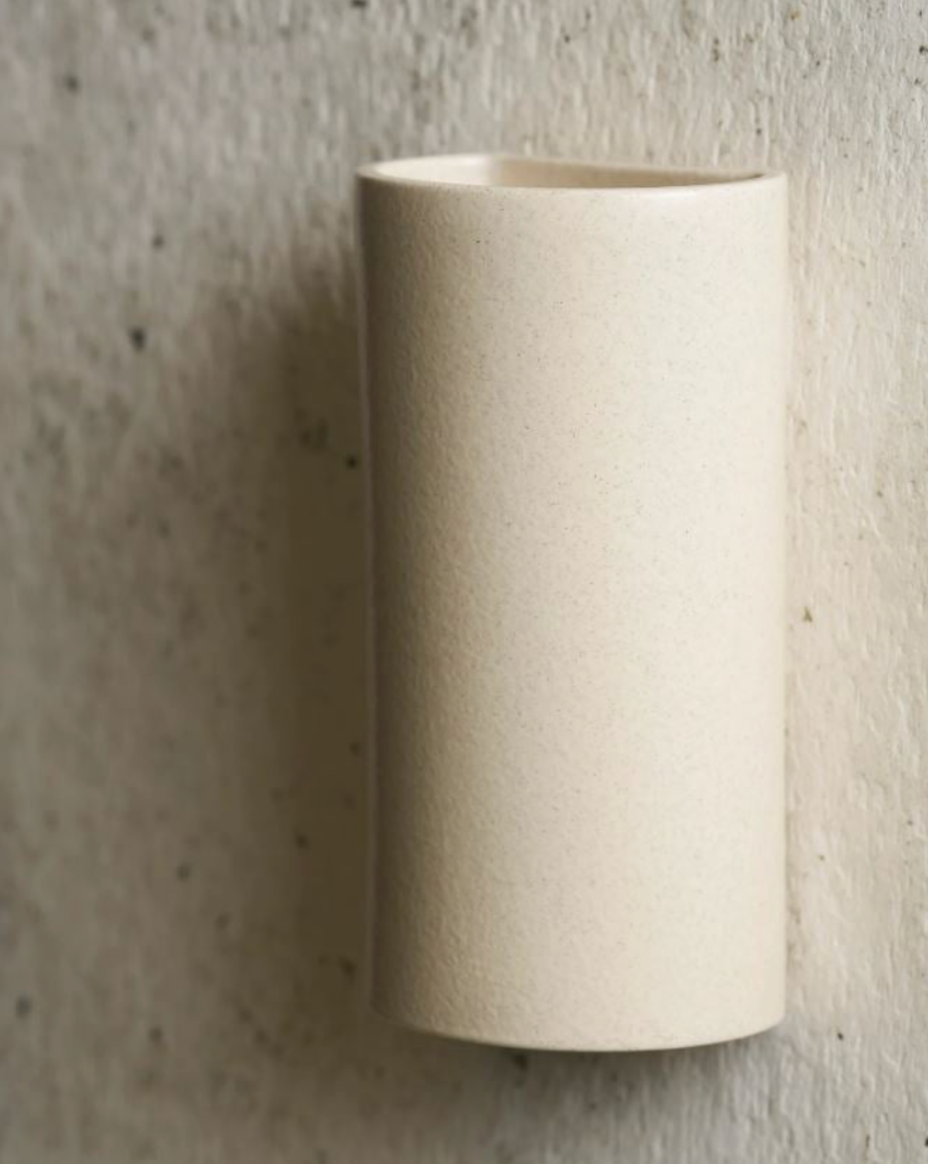 Speckled ceramic cylindrical wall-mounted light fixture on a textured grey wall