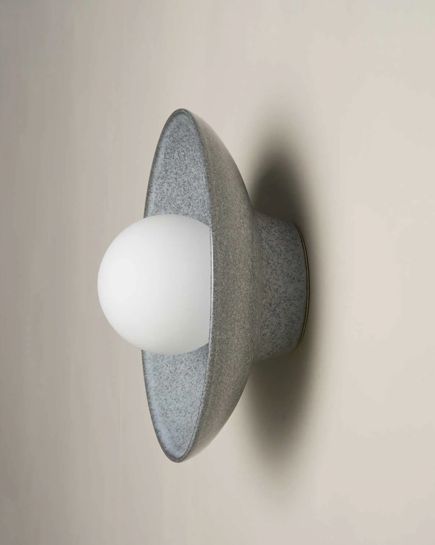 Wall-mounted light fixture with a textured ceramic base and white bulb on a neutral background