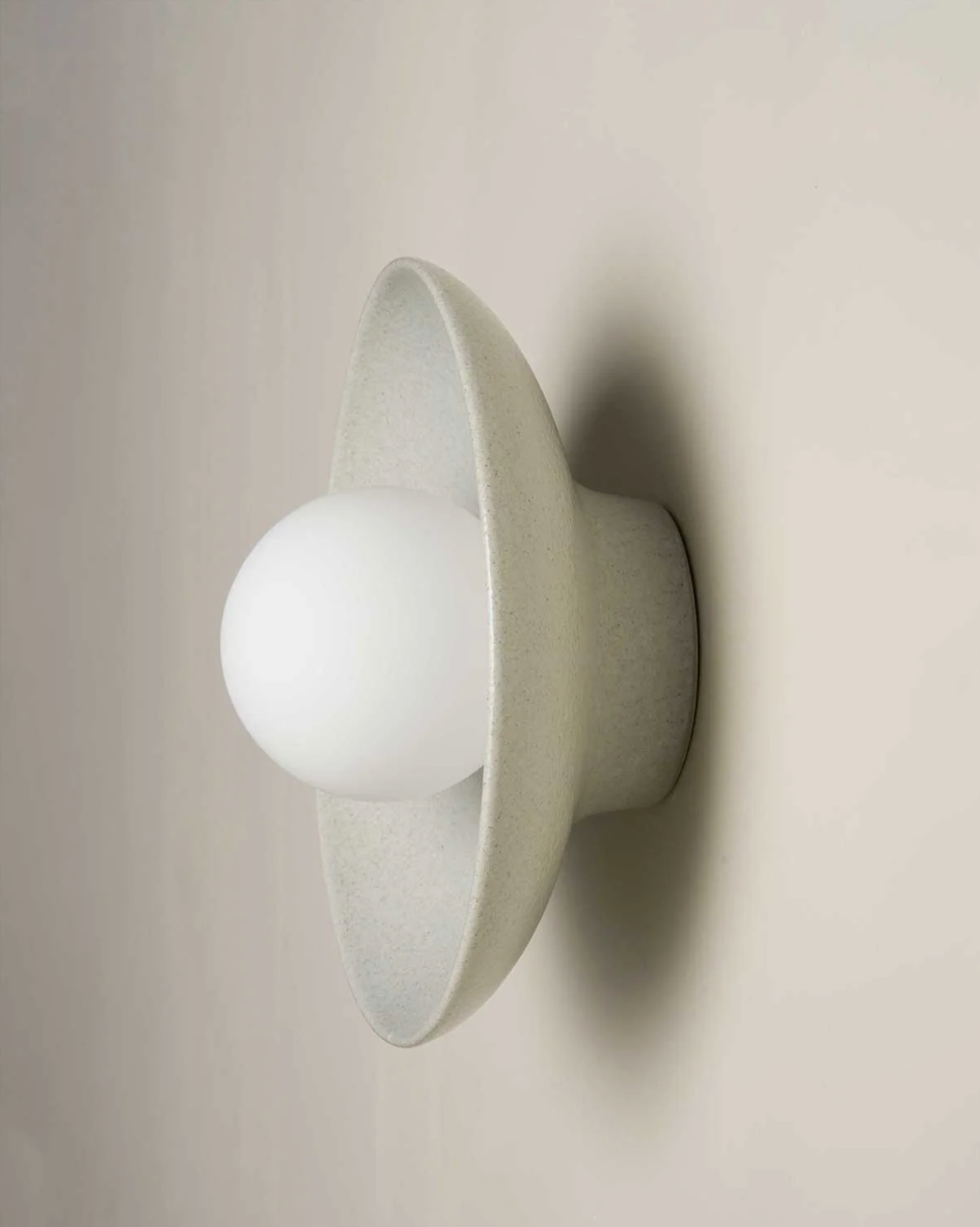 Wall-mounted ceramic light fixture with a white shade on a beige wall