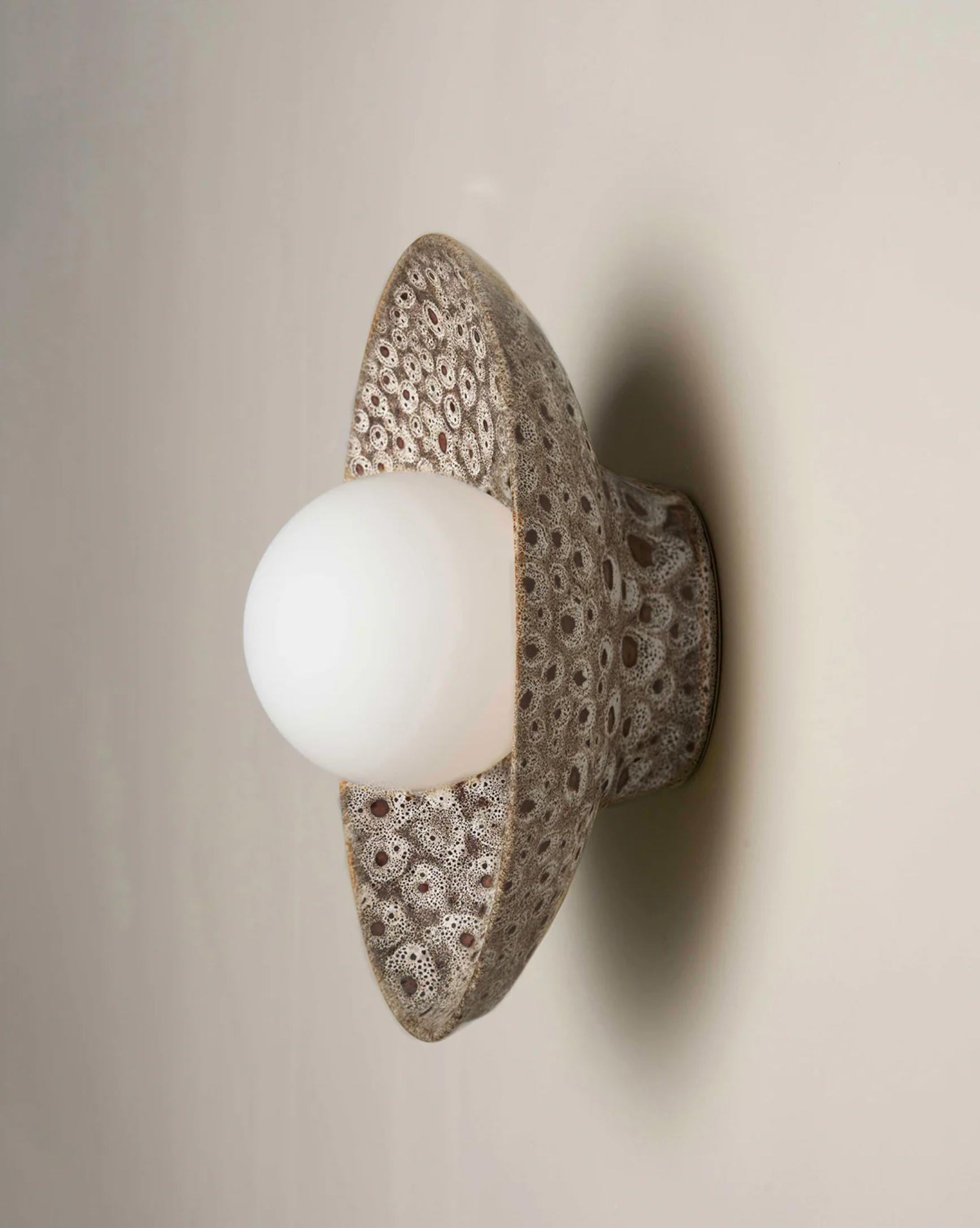 Decorative wall light fixture with textured ceramic casing and white bulb on a neutral background