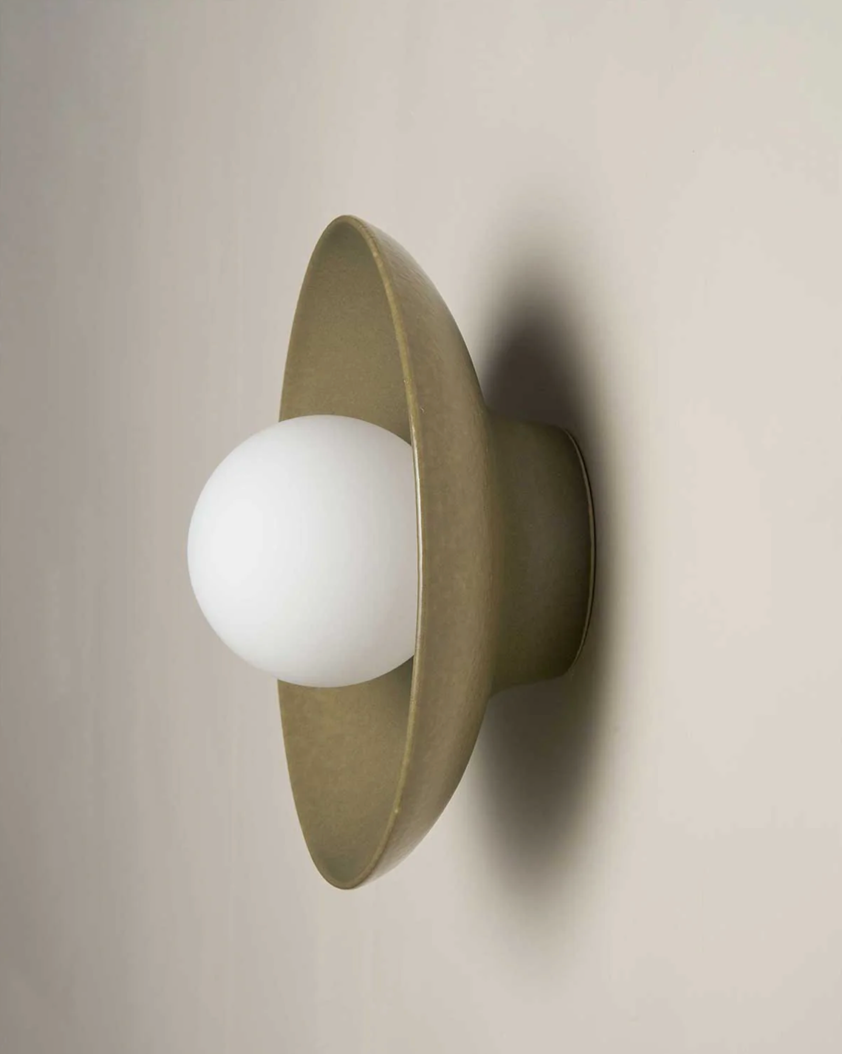Wall-mounted ceramic light fixture with a spherical bulb on a plain wall.