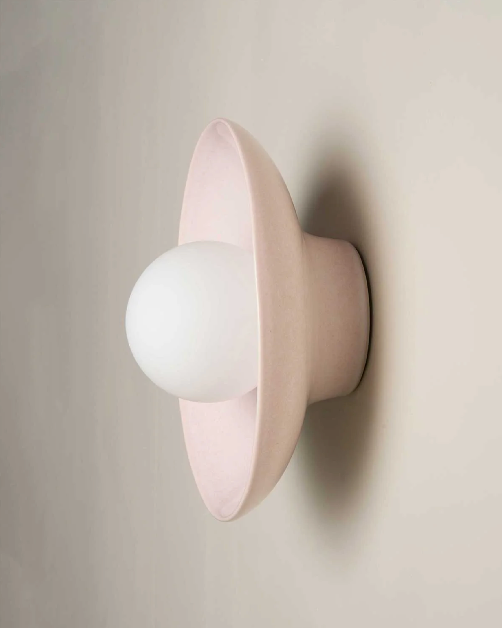 Light pink wall sconce with a white bulb on a beige background