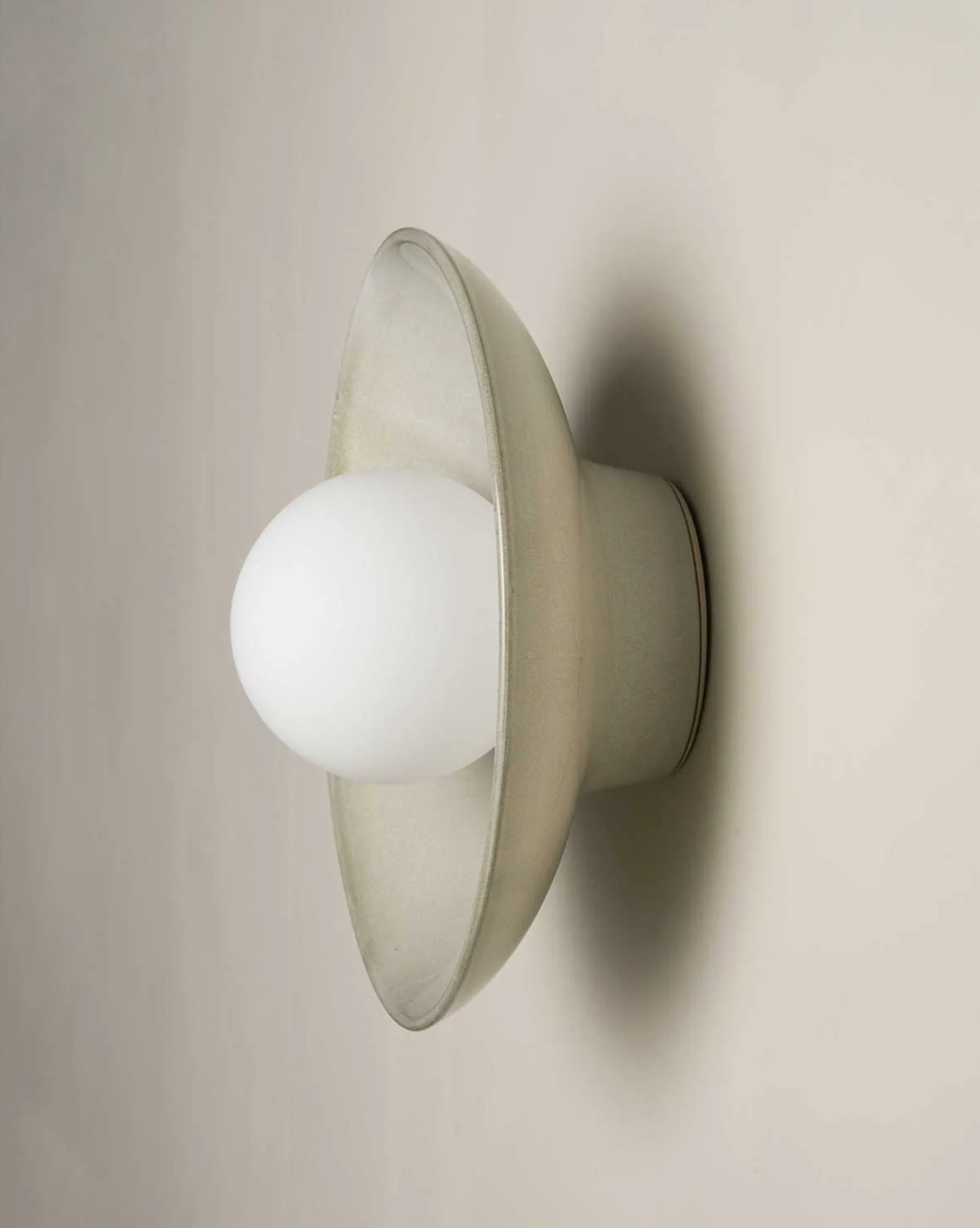 Wall-mounted ceramic light fixture with a white glass shade on a beige wall.