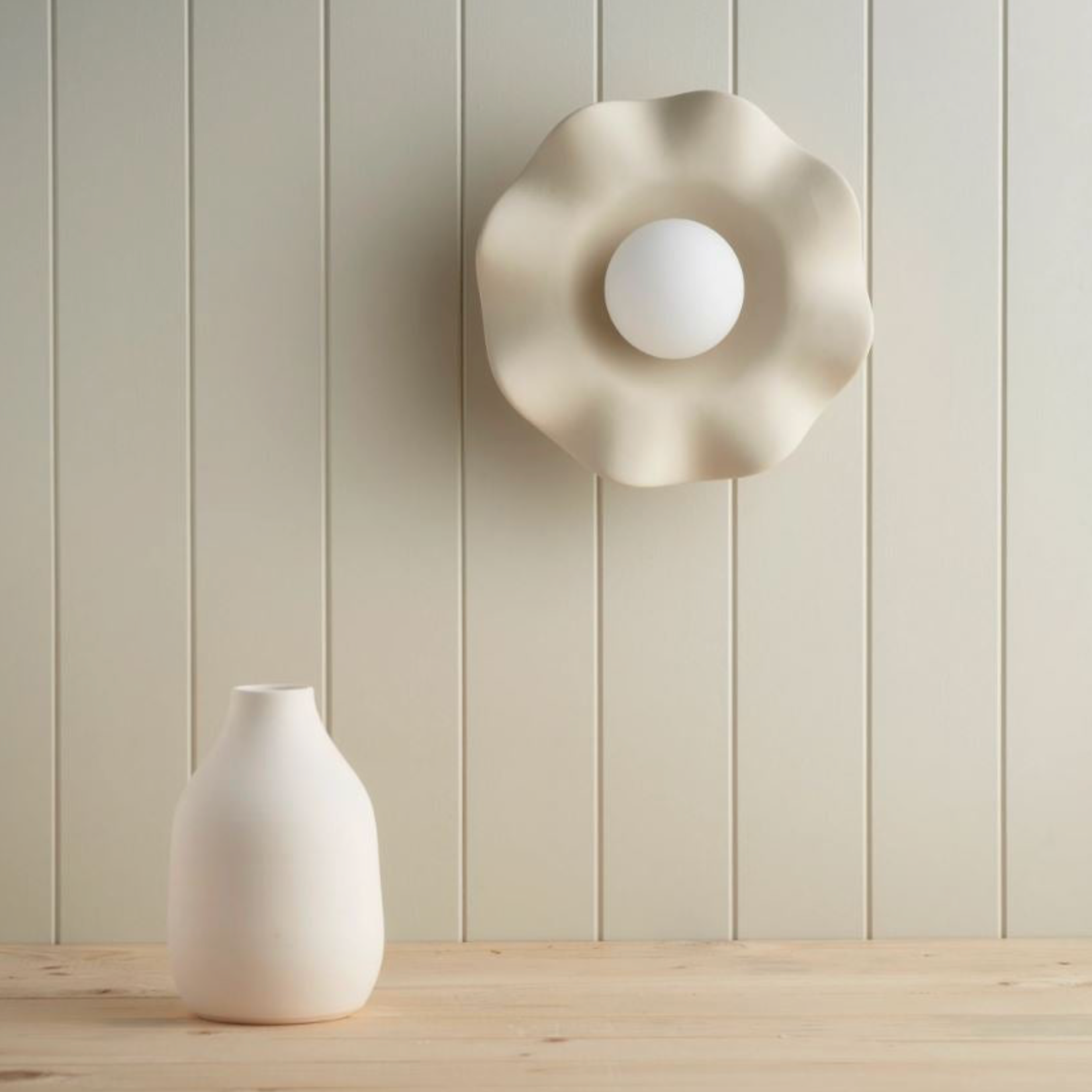 Decorative ceramic wall light fixture and white vase on a wooden surface with a light green paneled wall background.