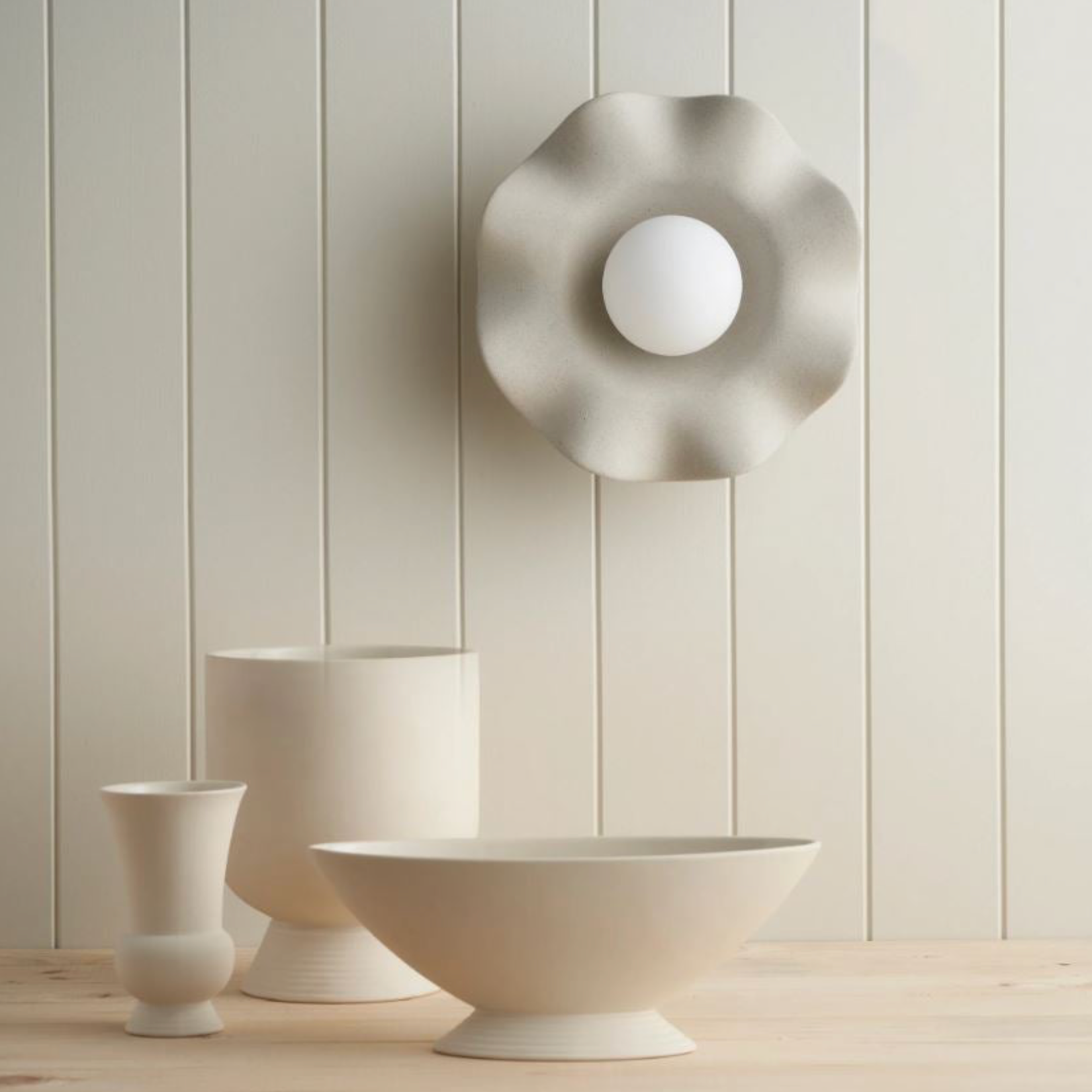 Decorative wall light fixture with three white ceramic vases against a light wooden panel background
