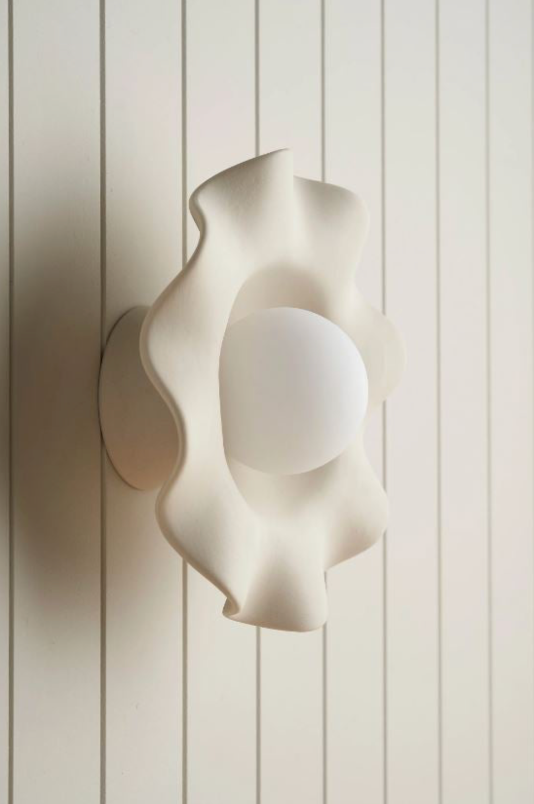 Modern ceramic wall lamp with a wavy design on a white panelled wall