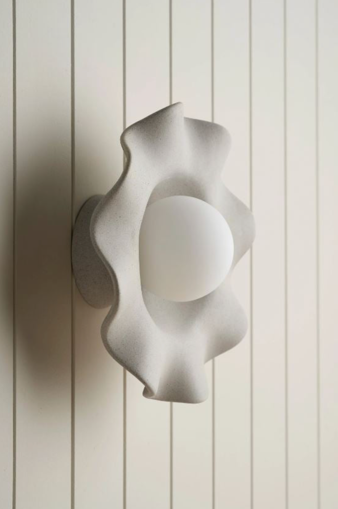 Modern wall sconce with a unique, organic design on a light wooden panel background