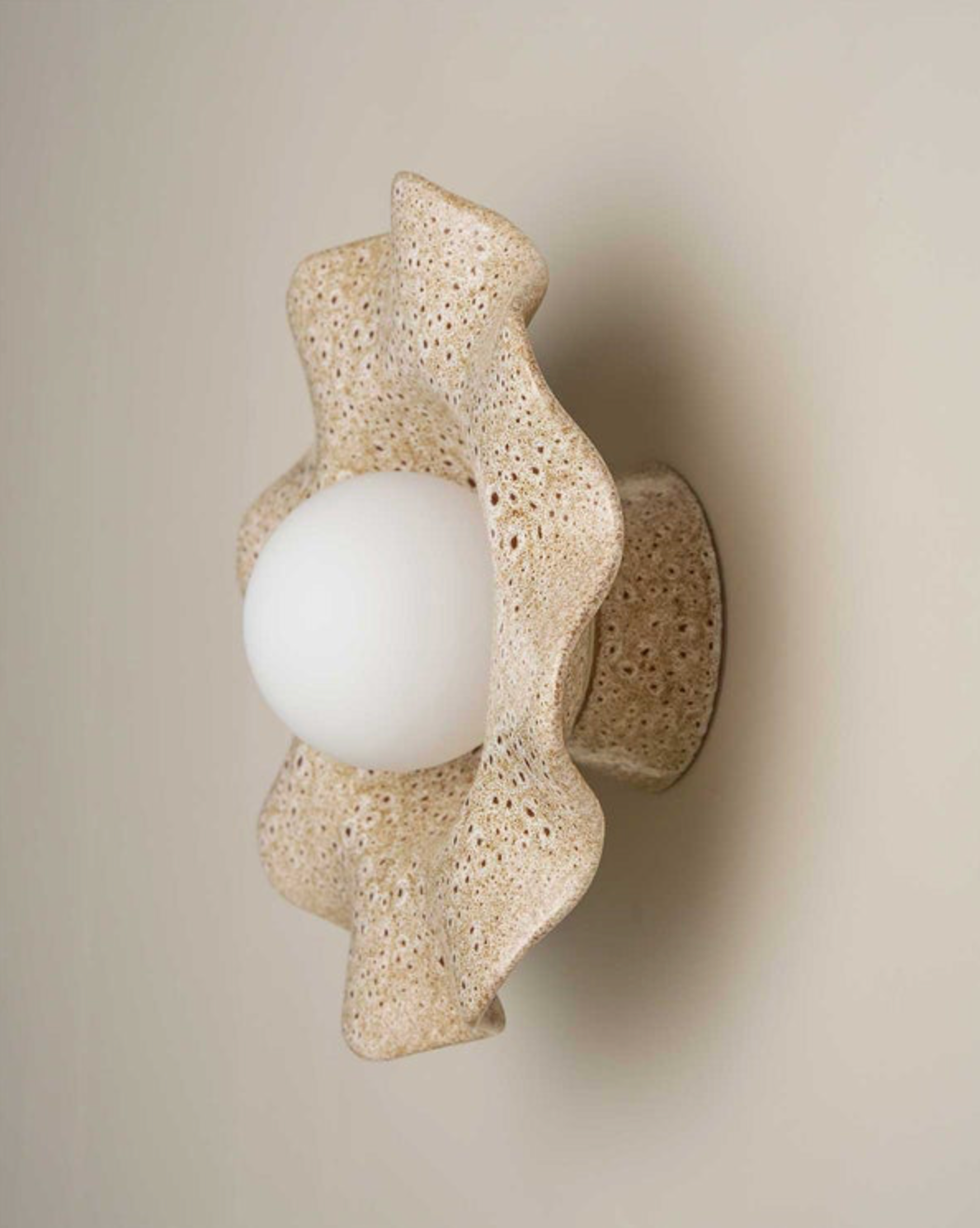 Ceramic wall sconce with a textured design on a beige wall.