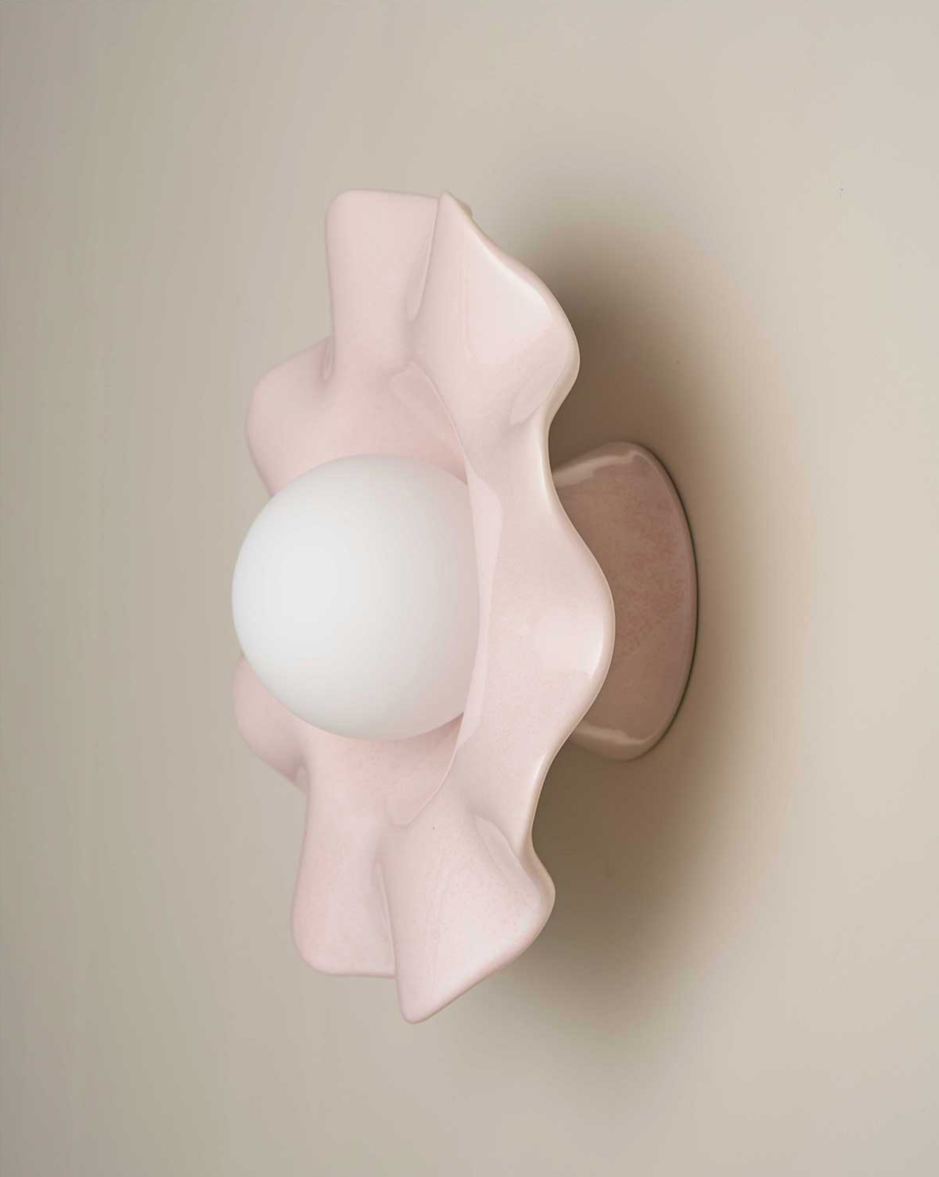 Pink ceramic wall sconce with a white bulb on a beige background
