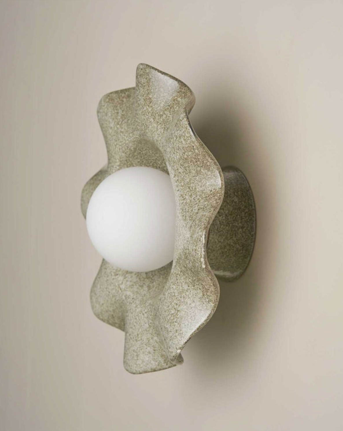 Decorative wall light fixture with a textured, wavy ceramic design on a beige background