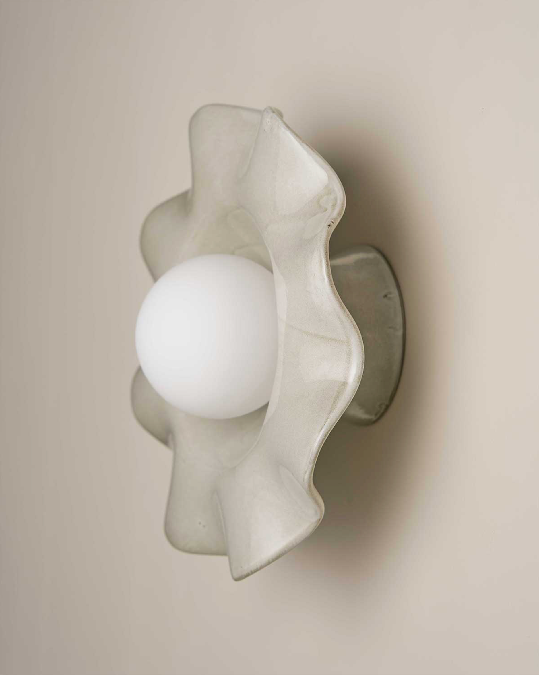 Spherical ceramic light fixture with wavy design on a beige wall