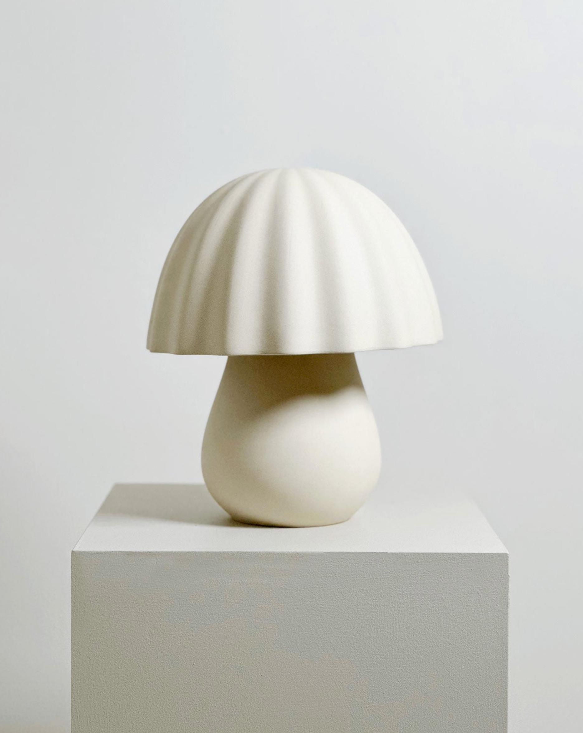 White ceramic table lamp on a grey pedestal against a light background