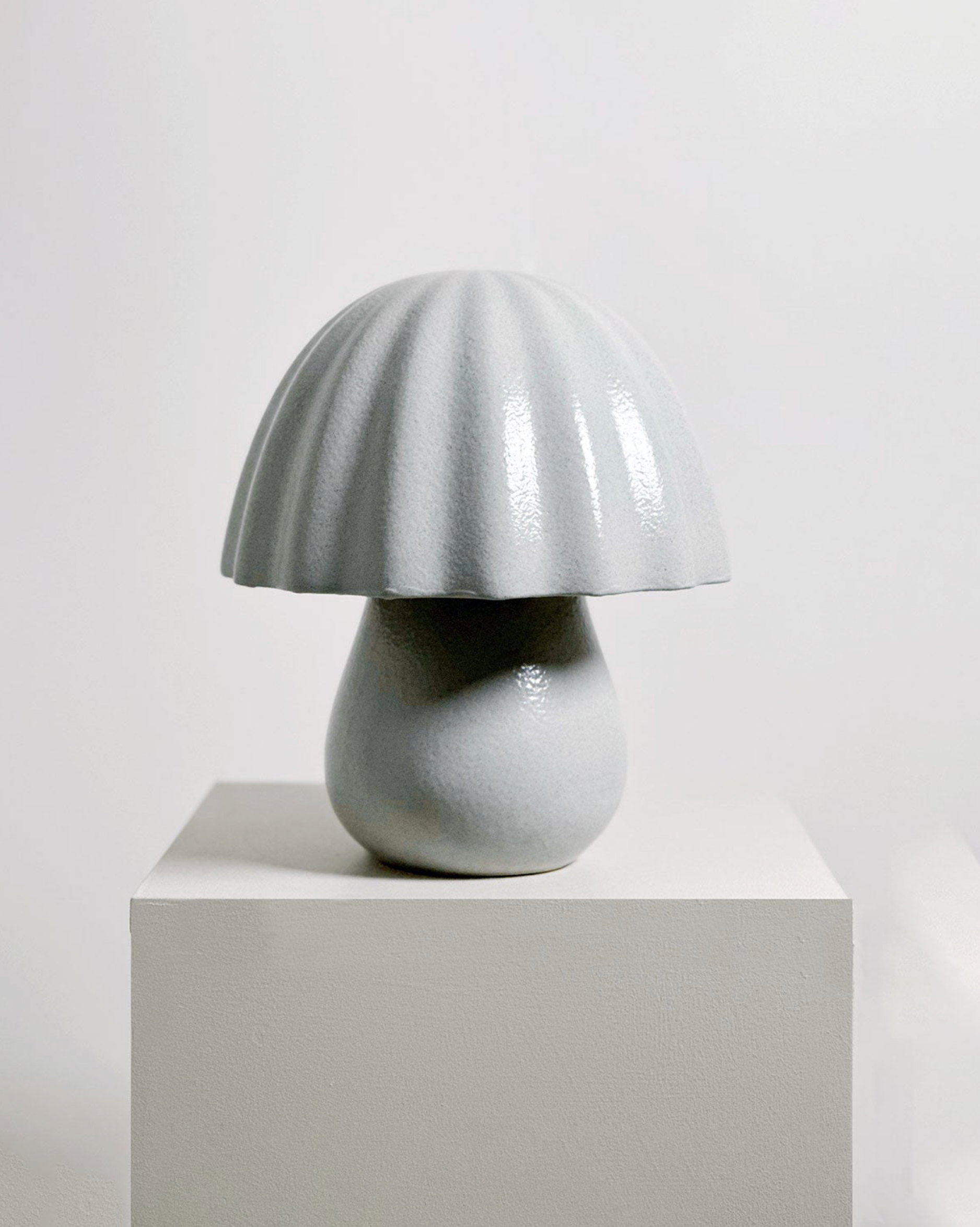 Ceramic mushroom-shaped lamp on a white pedestal against a light gray background