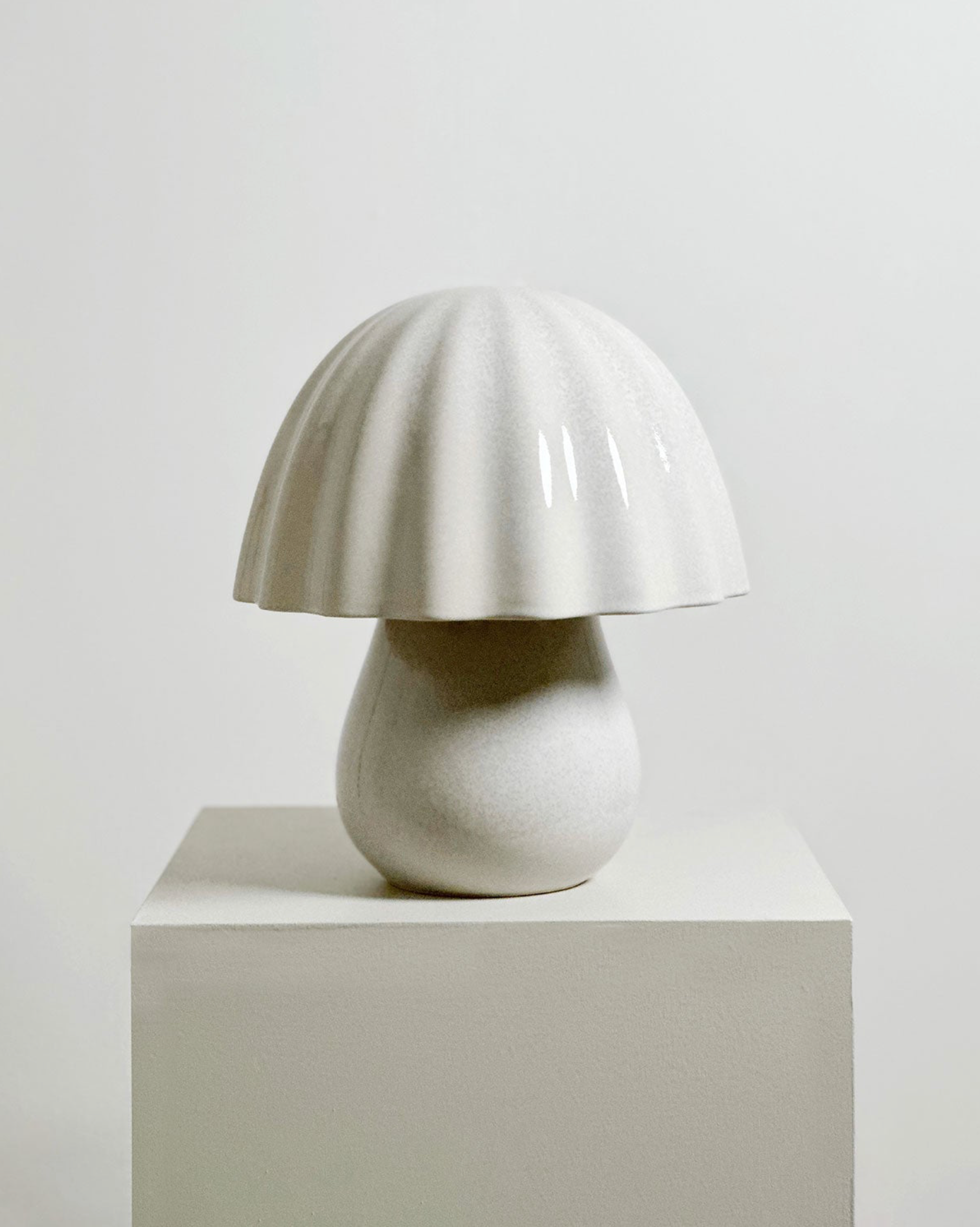 White ceramic lamp with a unique design on a light grey pedestal against a plain background