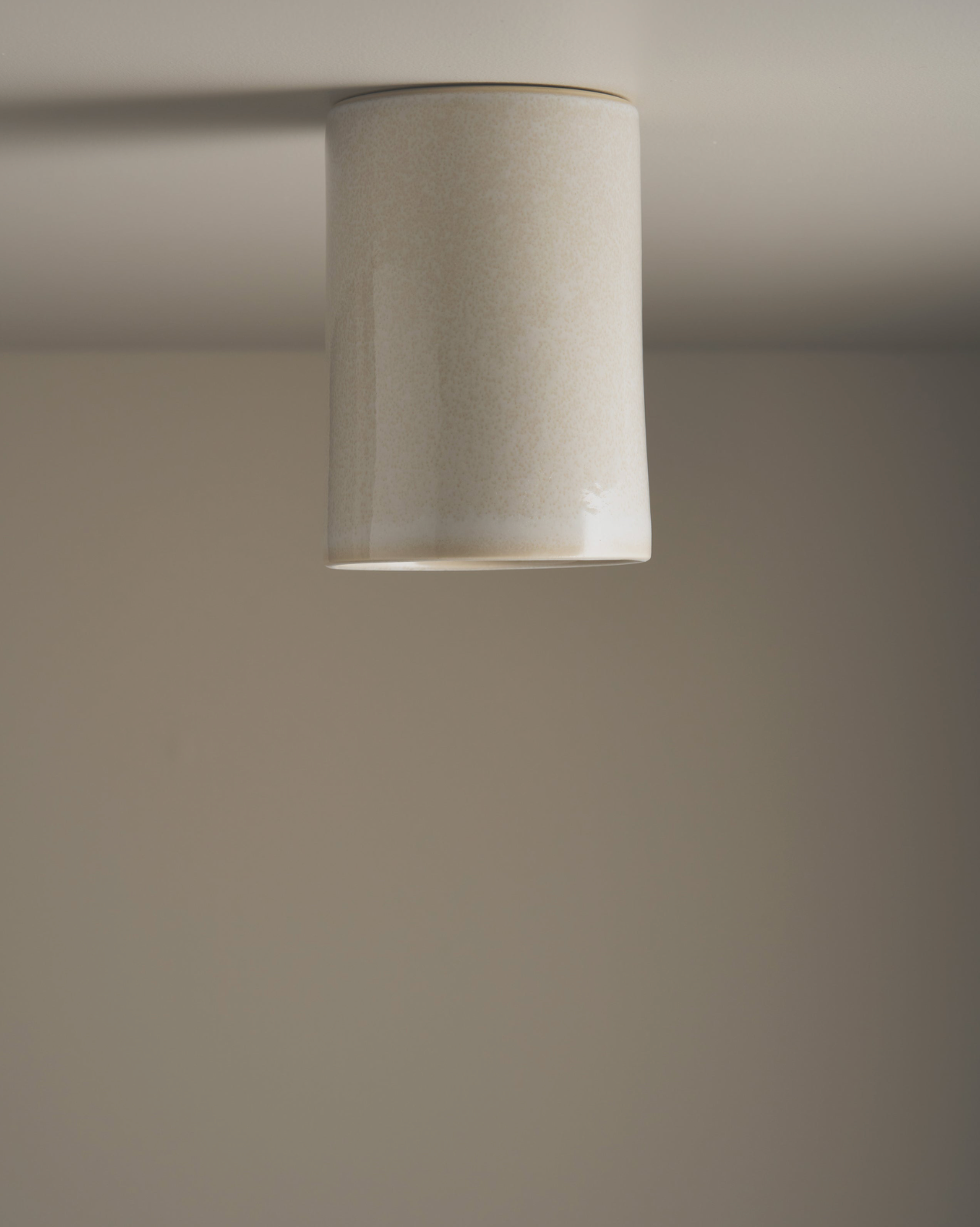 Ceramic interior ceiling light fixture with a cylindrical beige shade on a plain wall.