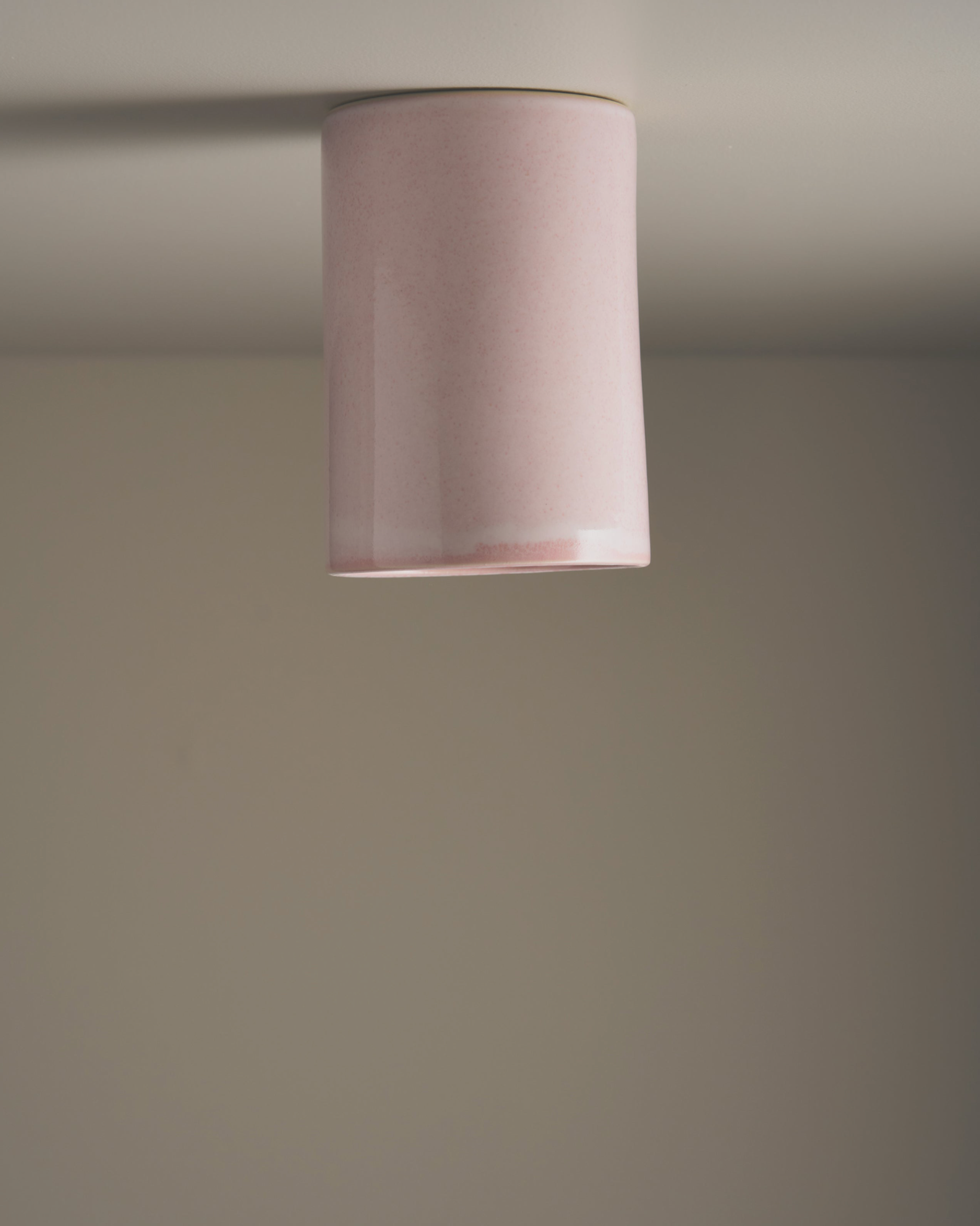 Ceiling light fixture with a cylindrical pink ceramic shade on a plain wall.