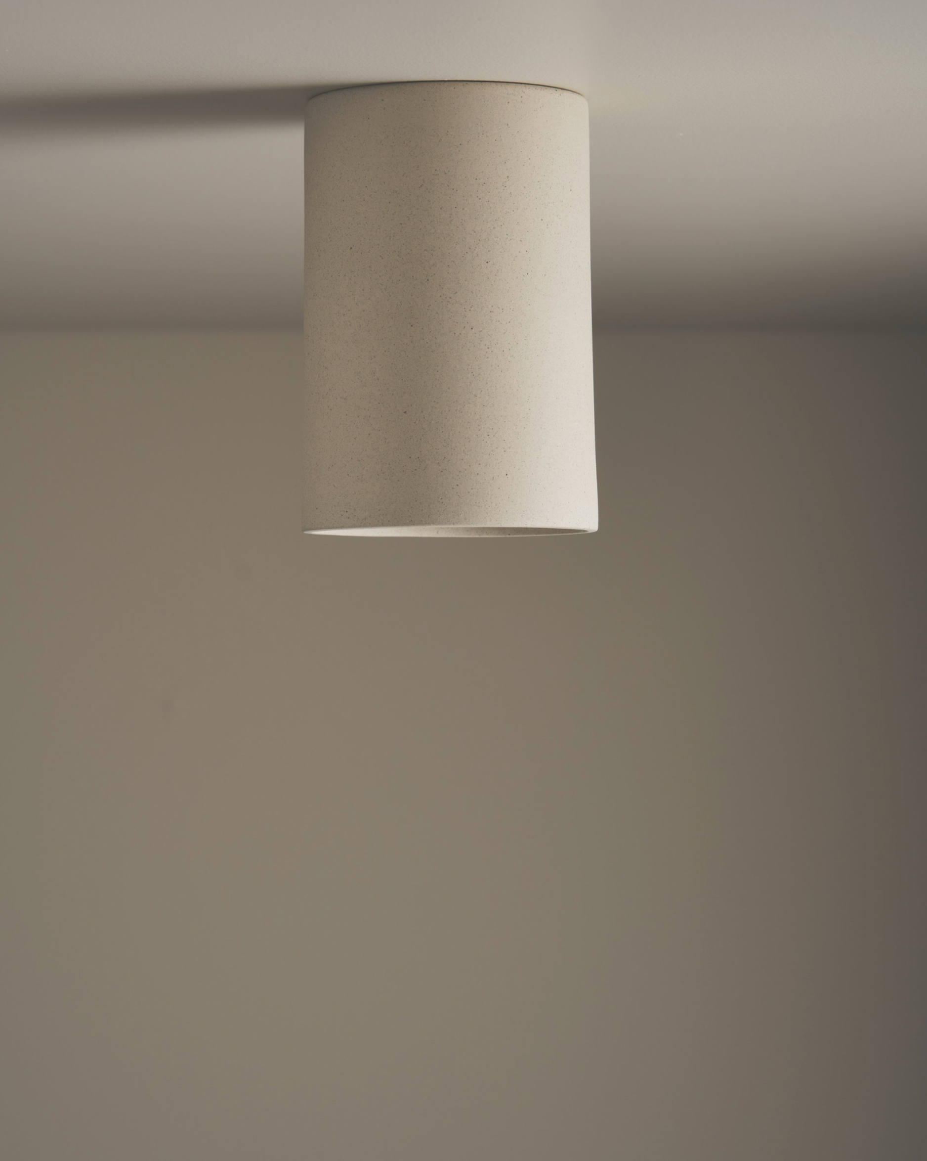 Ceiling light fixture with a cylindrical beige shade on a plain wall.