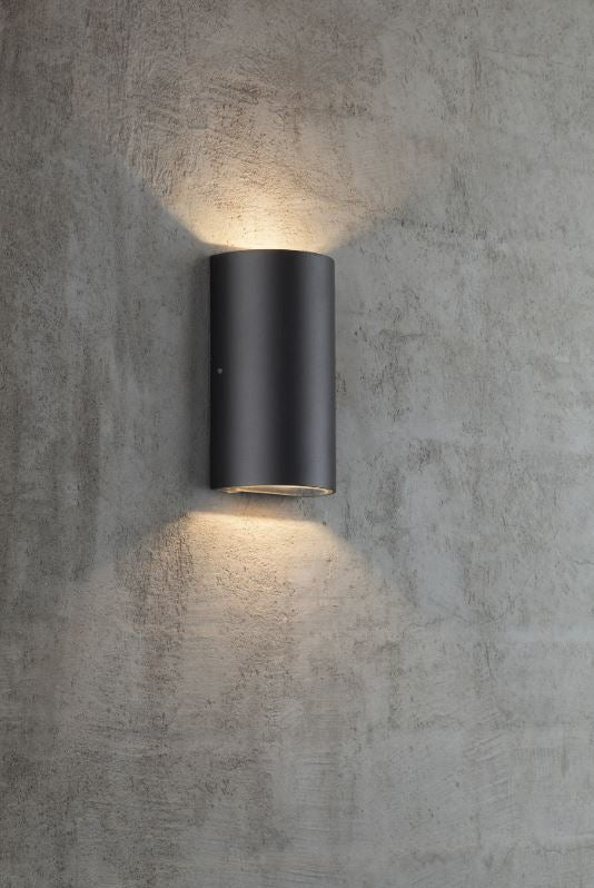 Black cylindrical outdoor wall light fixture on a concrete wall