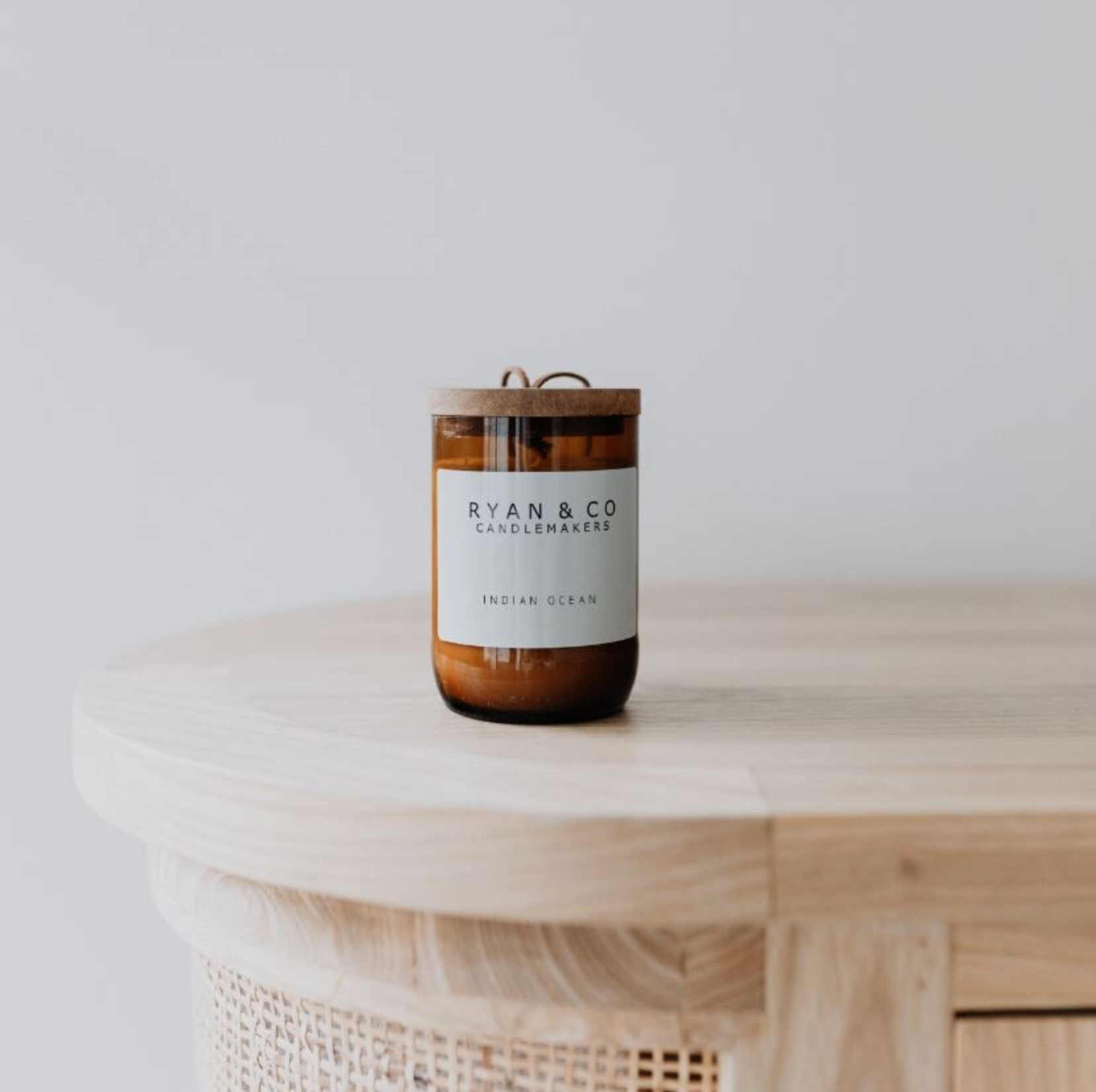 Candle with a wooden lid on a wicker surface against a light background