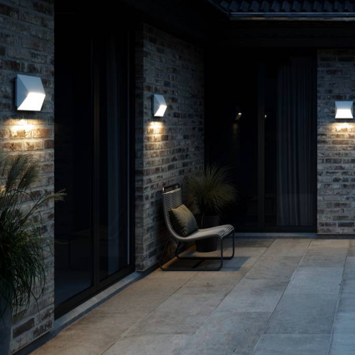 Modern outdoor setting with a chair against a brick wall illuminated by wall-mounted lights.