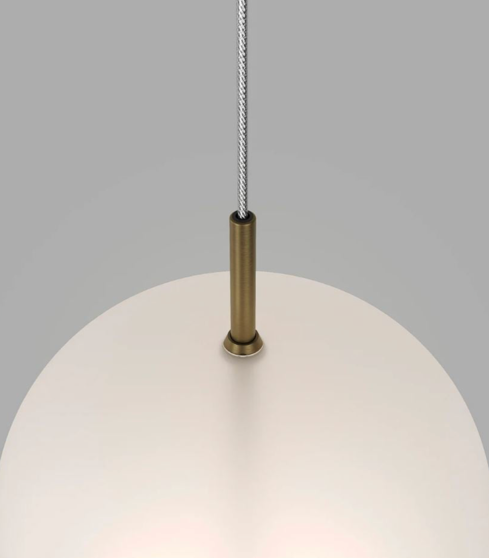 Close-up of a pendant light with a frosted glass shade and brass fitting on a gray background