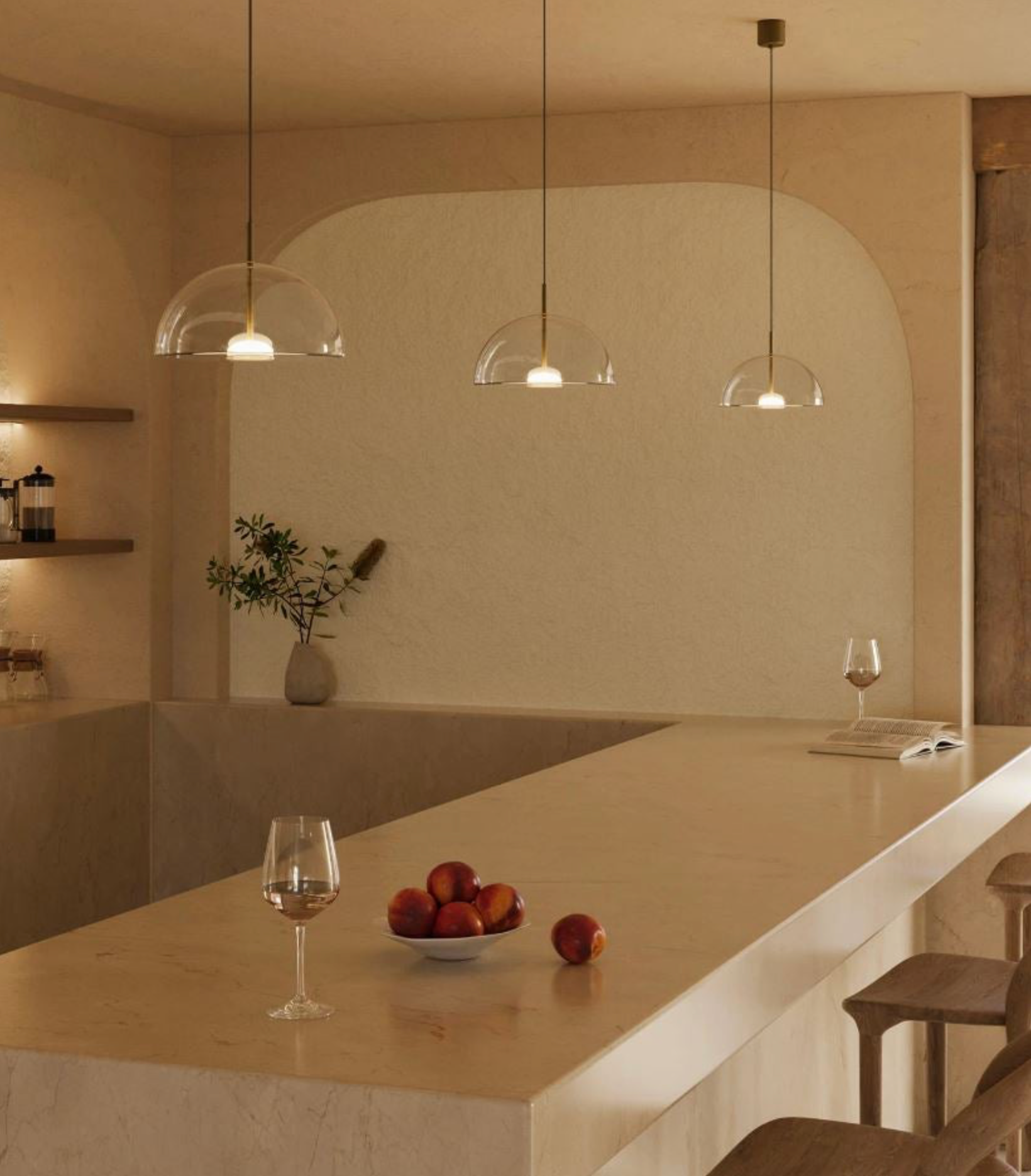 Modern kitchen with marble island, glass pendant lights, and a bowl of fruit.