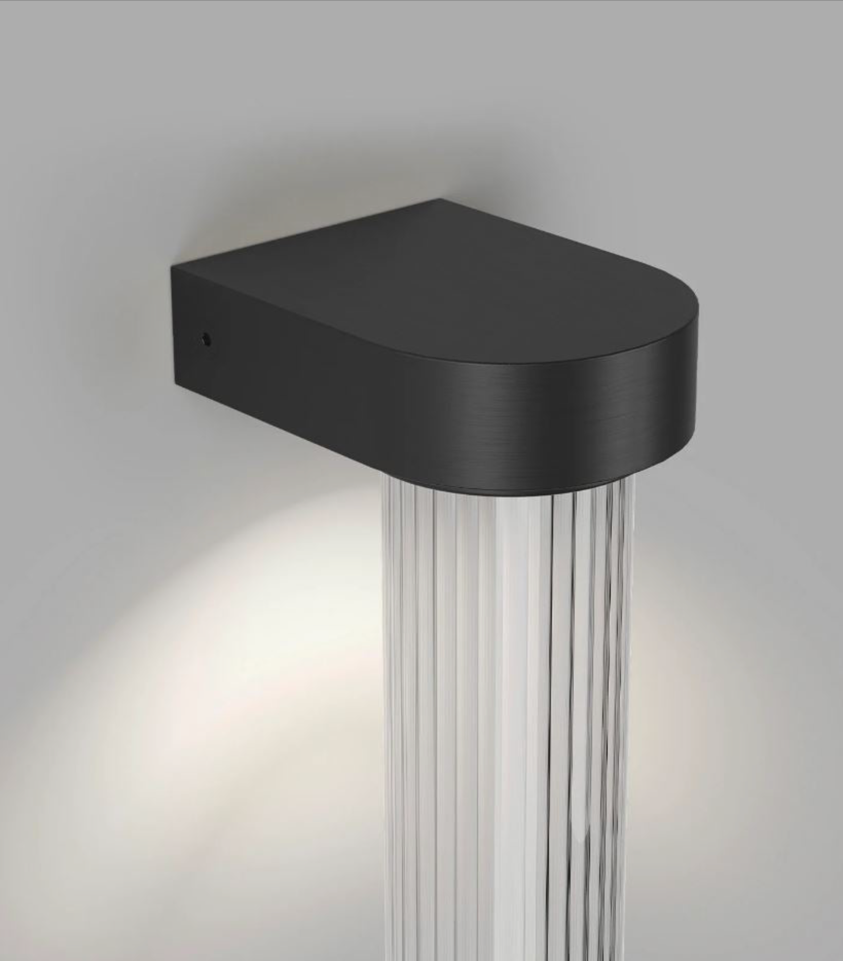 Black wall-mounted light fixture with cylindrical glass diffuser on a grey background