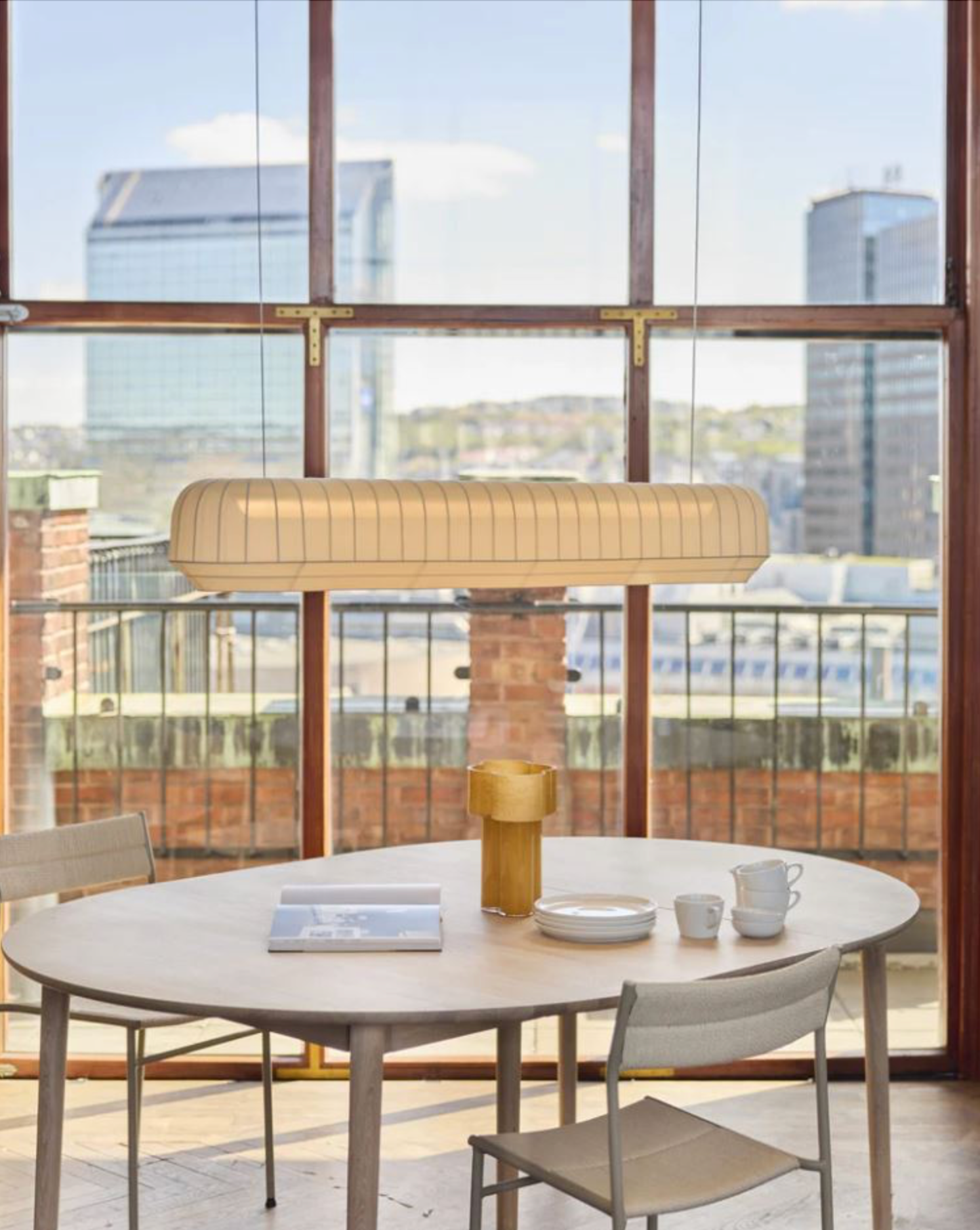 Modern dining area with linear pendant light over a round table and chairs in front of large windows with cityscape view