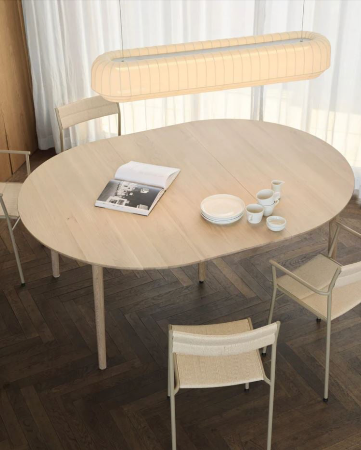 Round wooden dining table with chairs and a linear pendant light in a room with large windows.