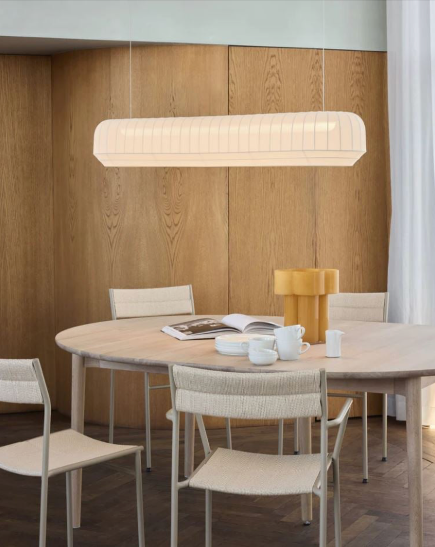 Dining area with a round table, chairs, and a pendant light in a room with wooden walls.