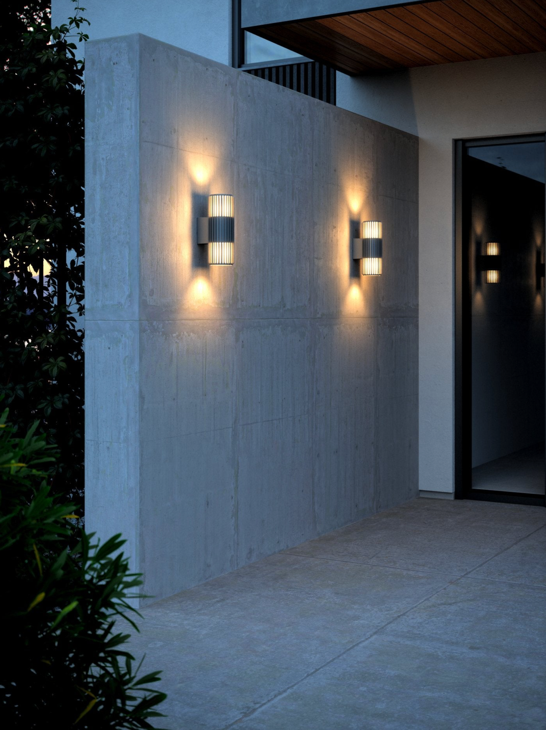 Modern outdoor wall lights on a concrete wall with a building entrance in the background.