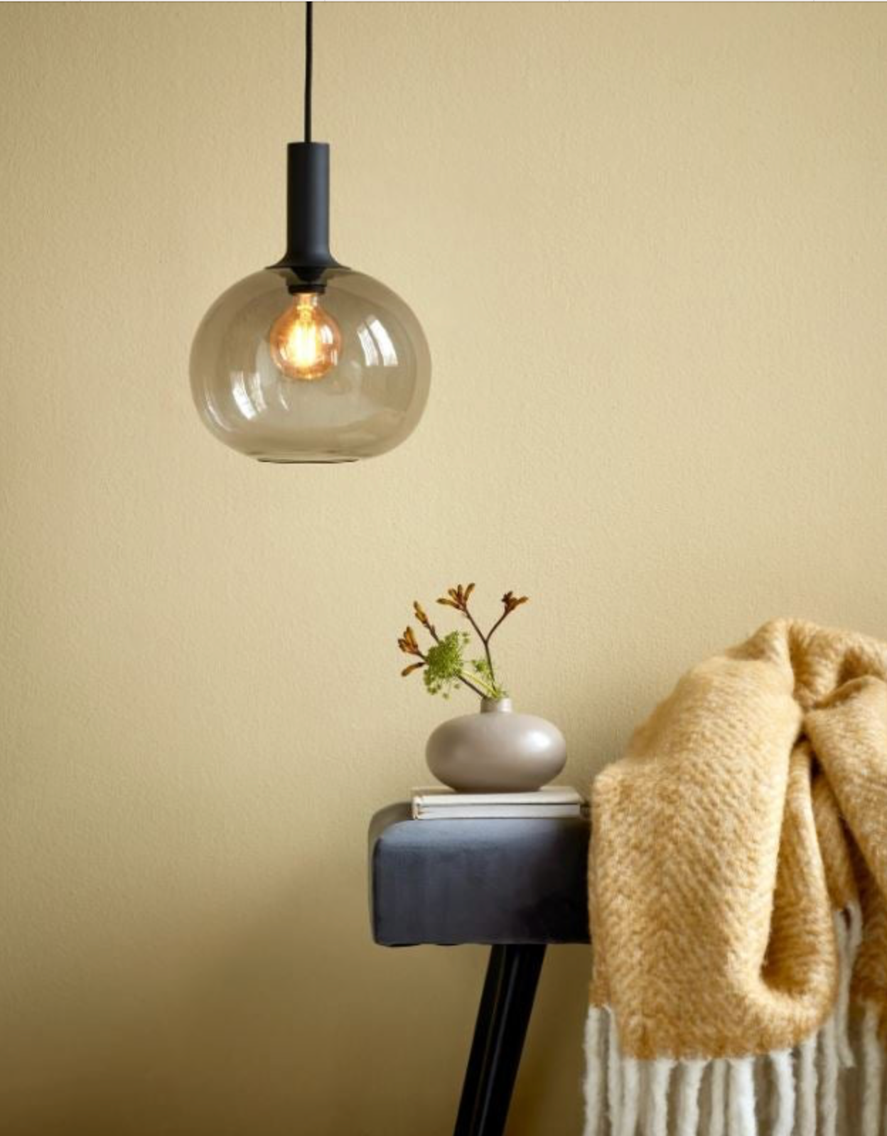 Pendant light fixture with a smokey glass shade on a beige wall.