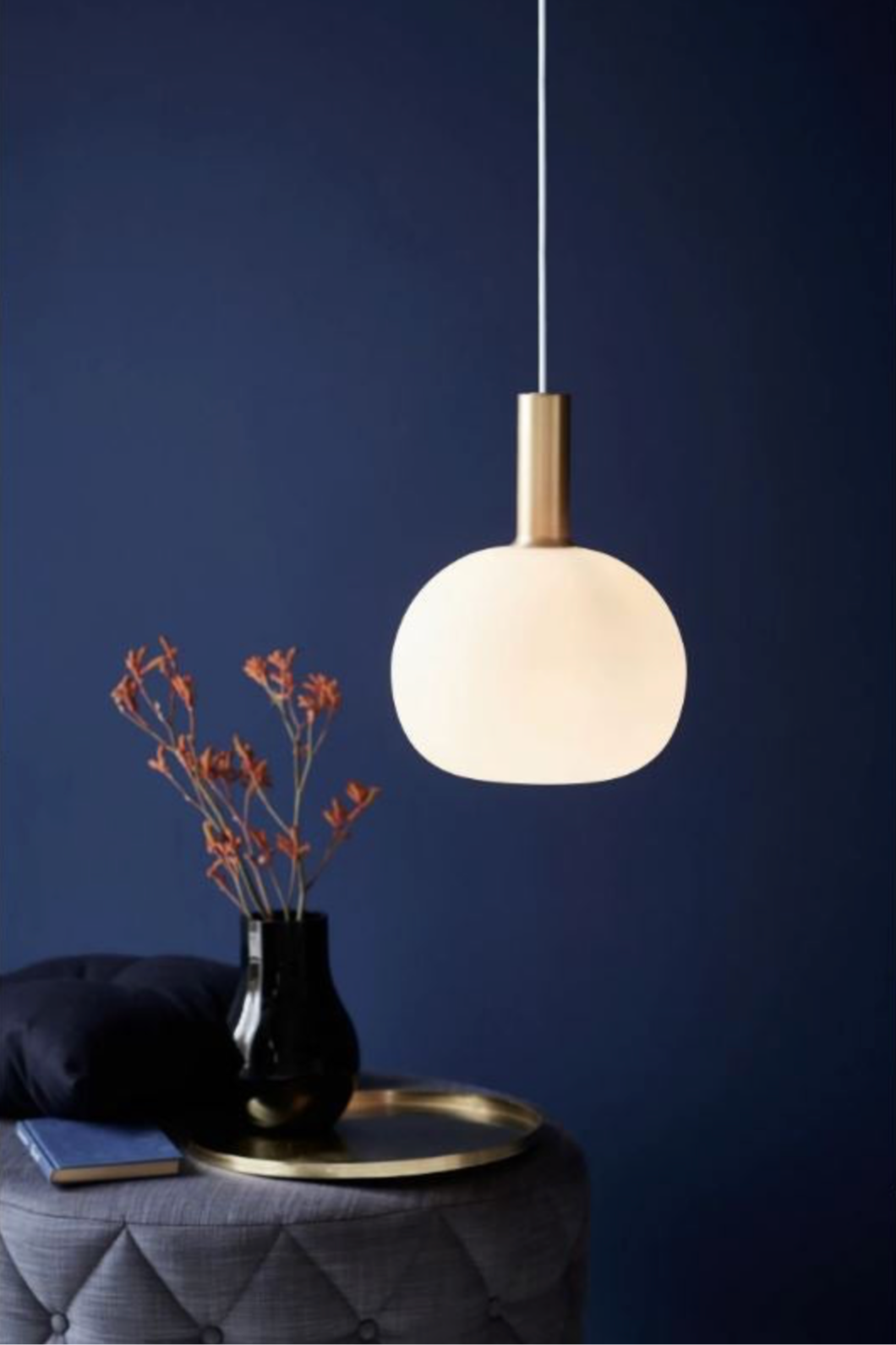 Pendant light fixture hanging against a dark blue wall with a vase and decorative items on a table.