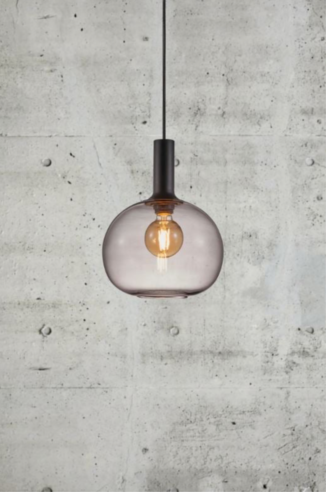 Modern pendant light with a glass shade against a concrete wall.