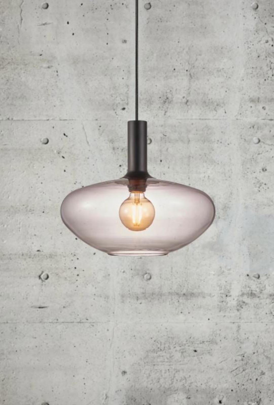 Modern pendant light with a glass shade against a concrete wall.