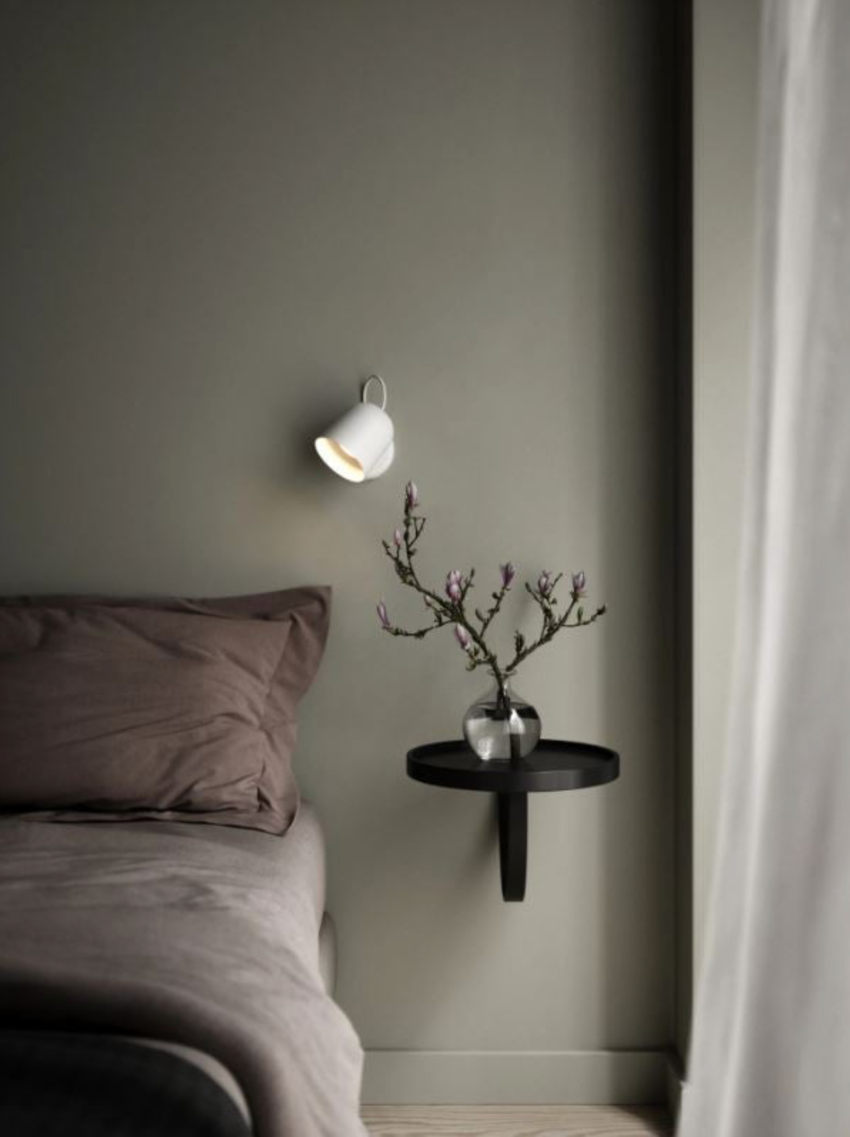 Modern bedroom with a wall-mounted lamp and small round table against a gray wall.