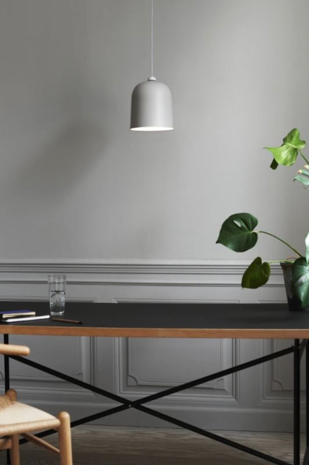 Modern interior with a black desk, grey pendant light, and green plant against a grey wall.