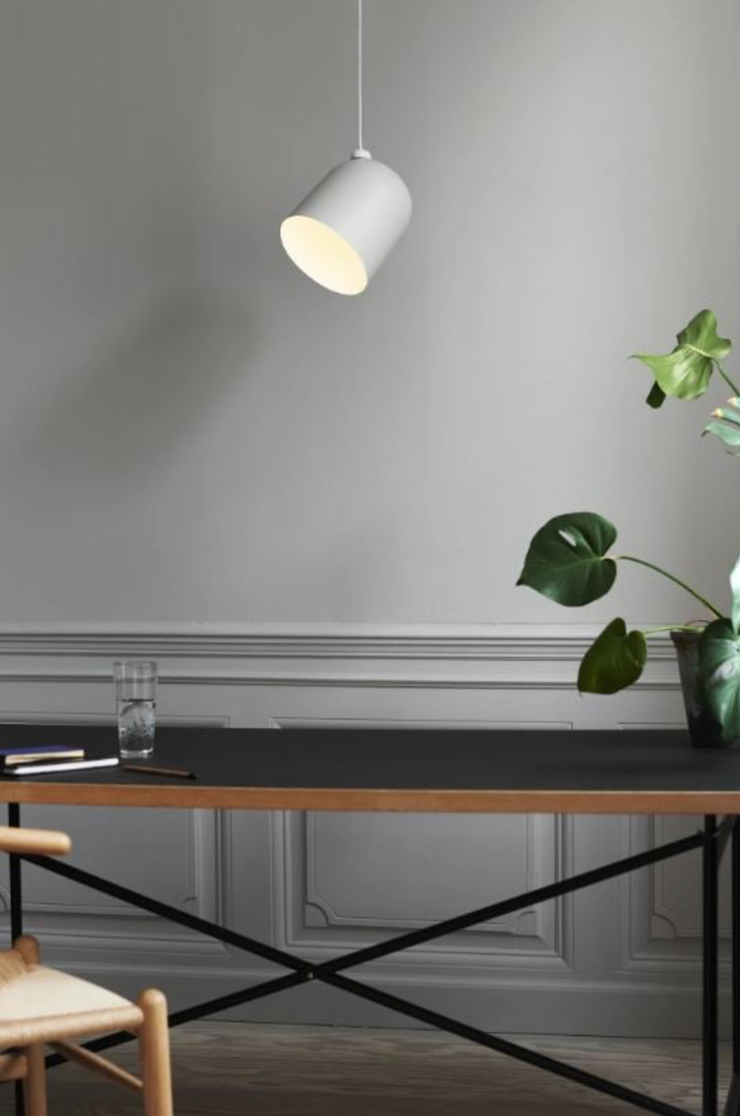 Modern interior with a black desk, white pendant light, and green plant against a grey wall.