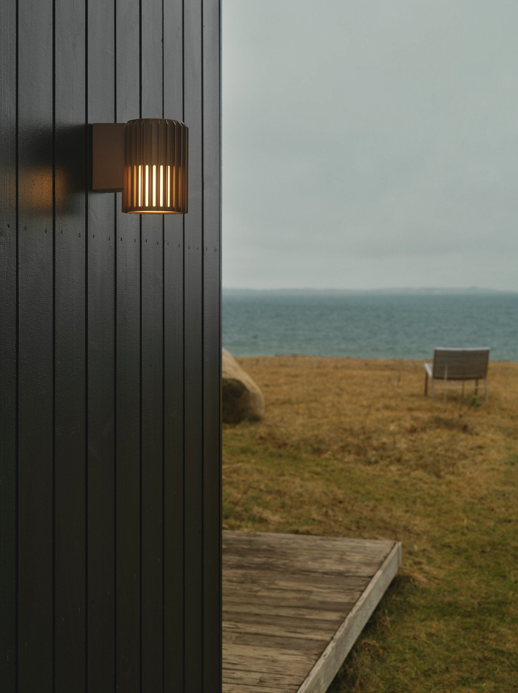 Outdoor wall light fixture on a building with a scenic view of the ocean and grassy area.