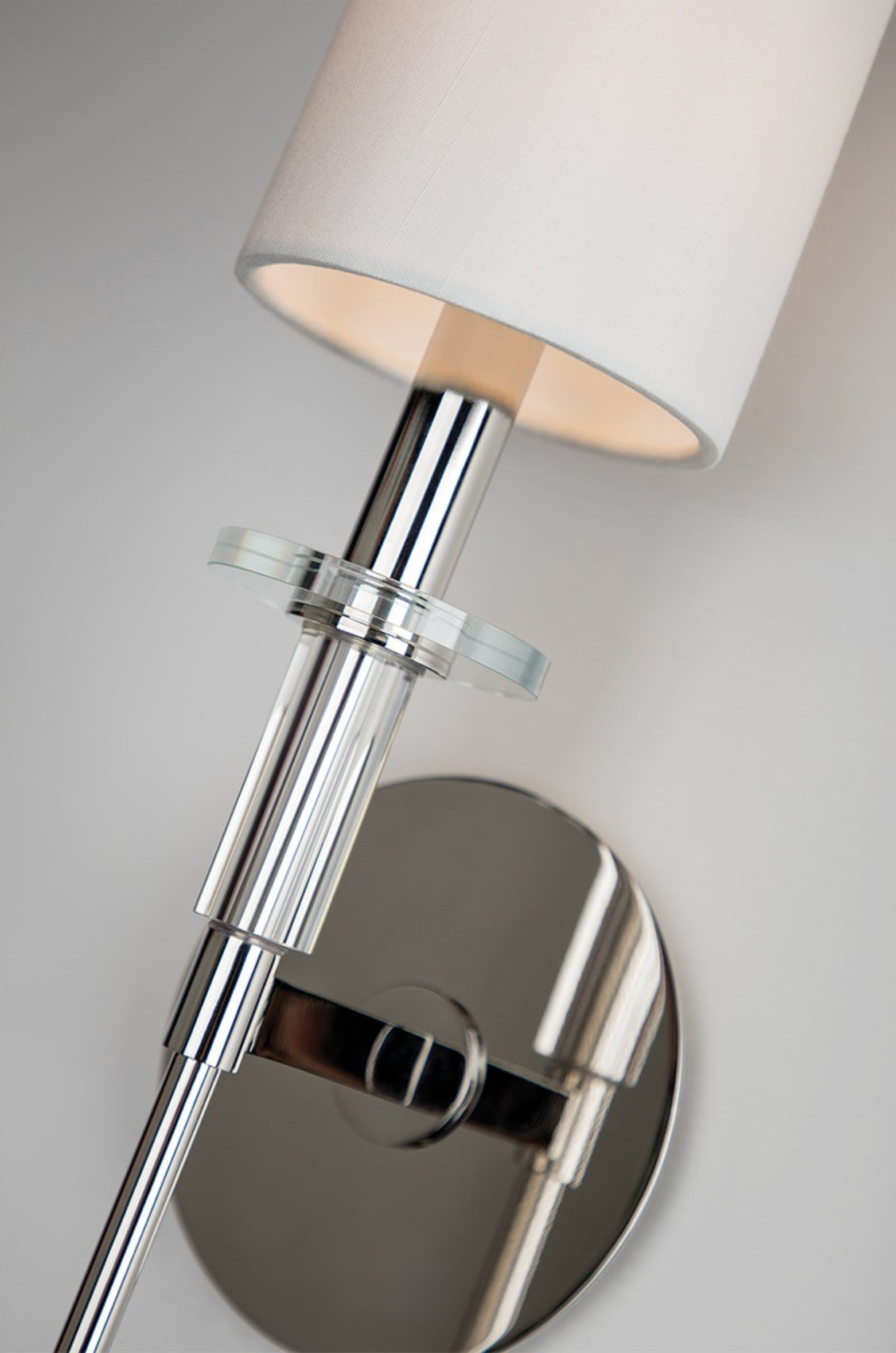 Chrome wall sconce with a white lampshade on a neutral background