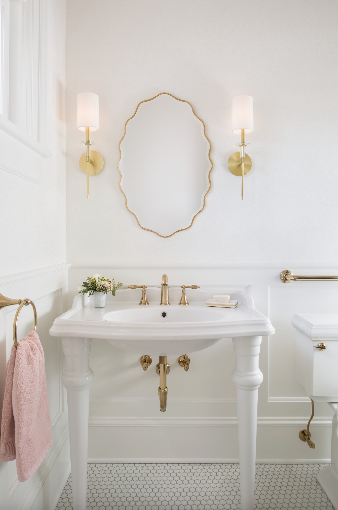 Bathroom with white sink, gold wall light fixtures, and decorative mirror.