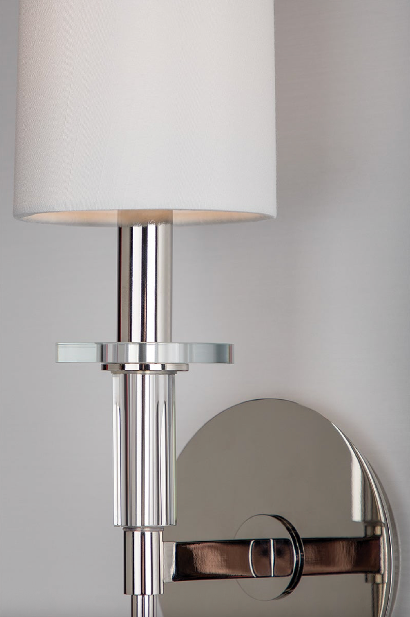 Chrome wall sconce with a white lampshade on a neutral background