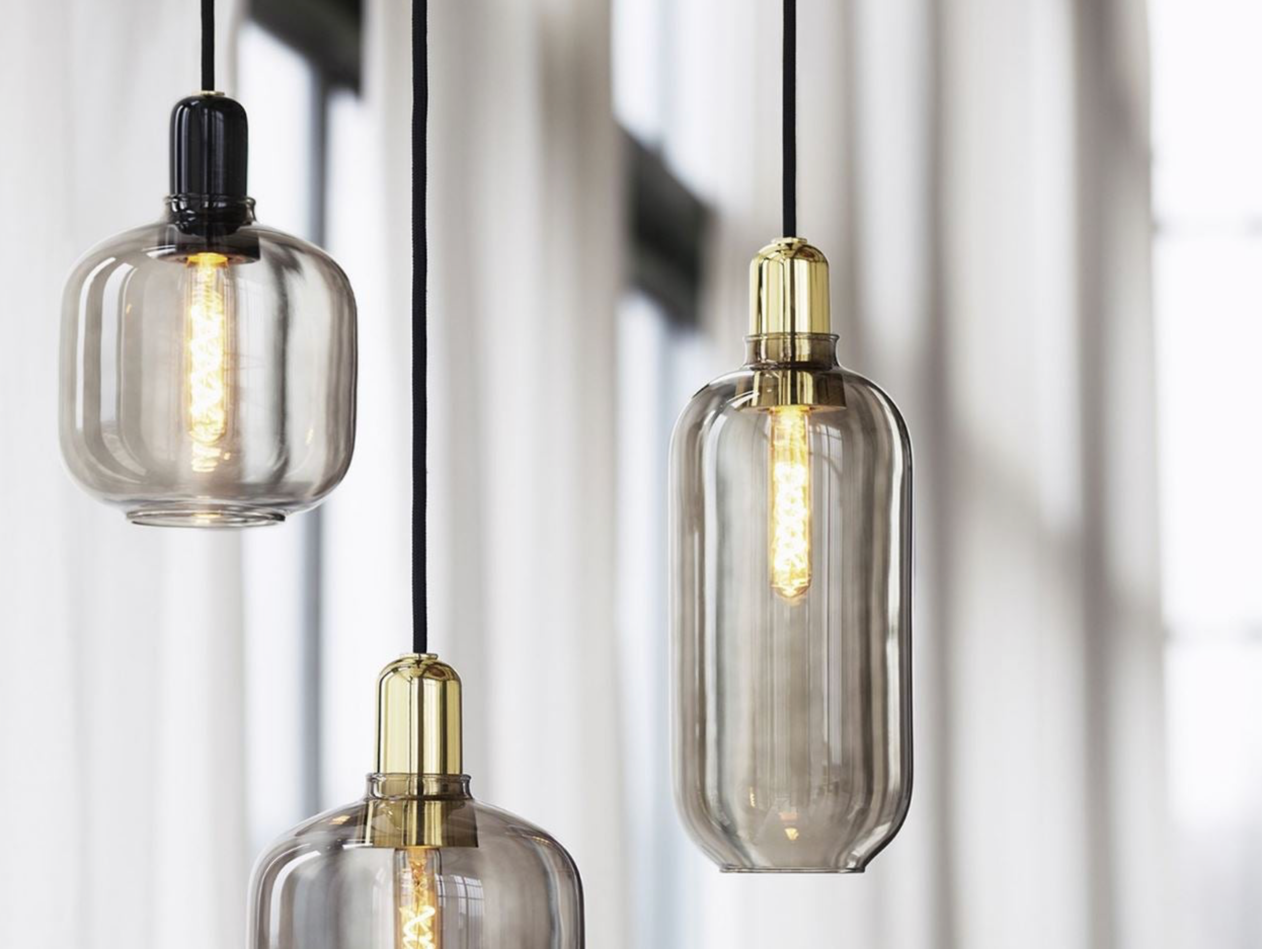 Three pendant lights with glass shades and gold fixtures against a neutral background
