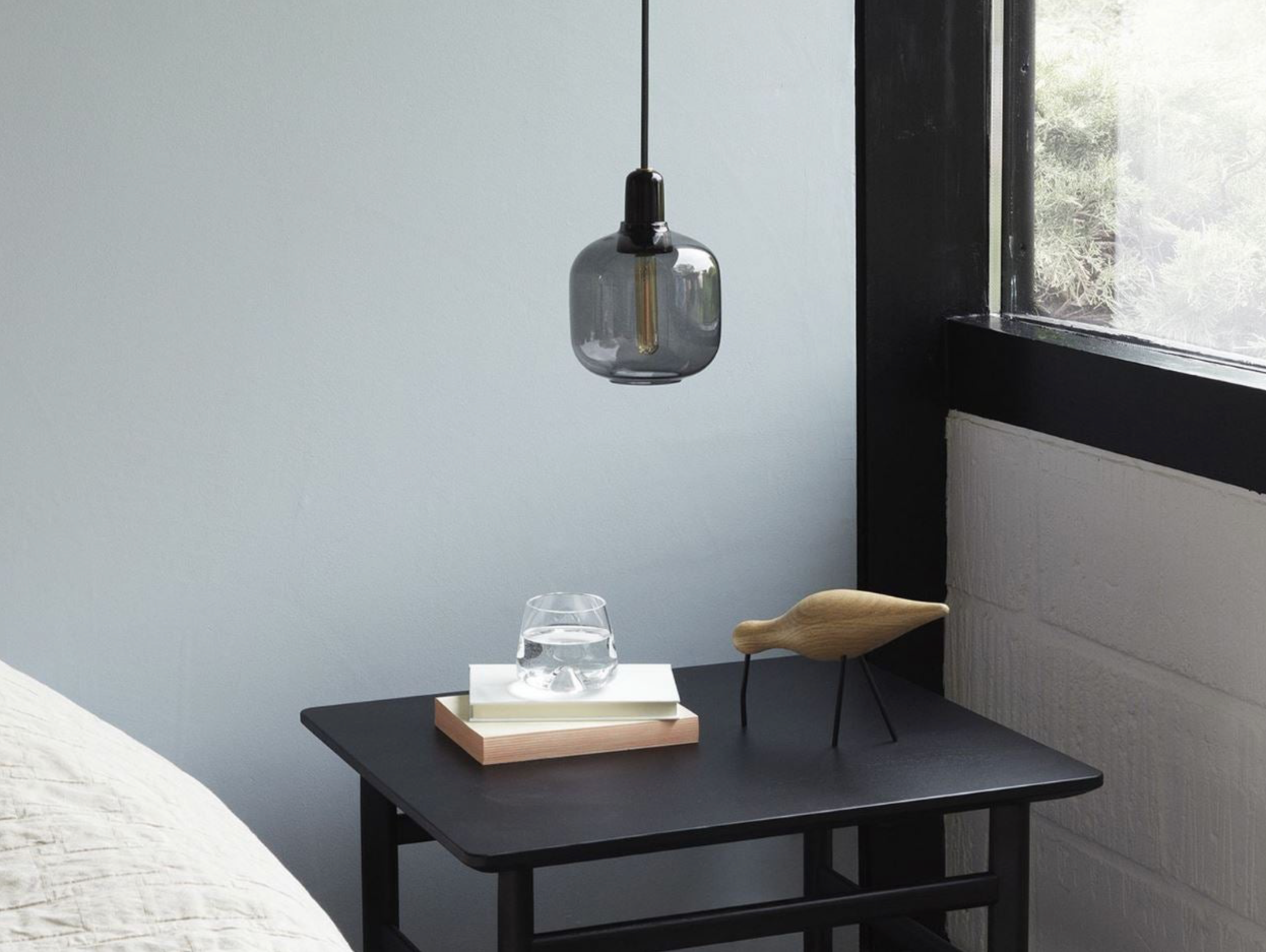 Modern bedroom with a black nightstand, pendant light, and decorative items.