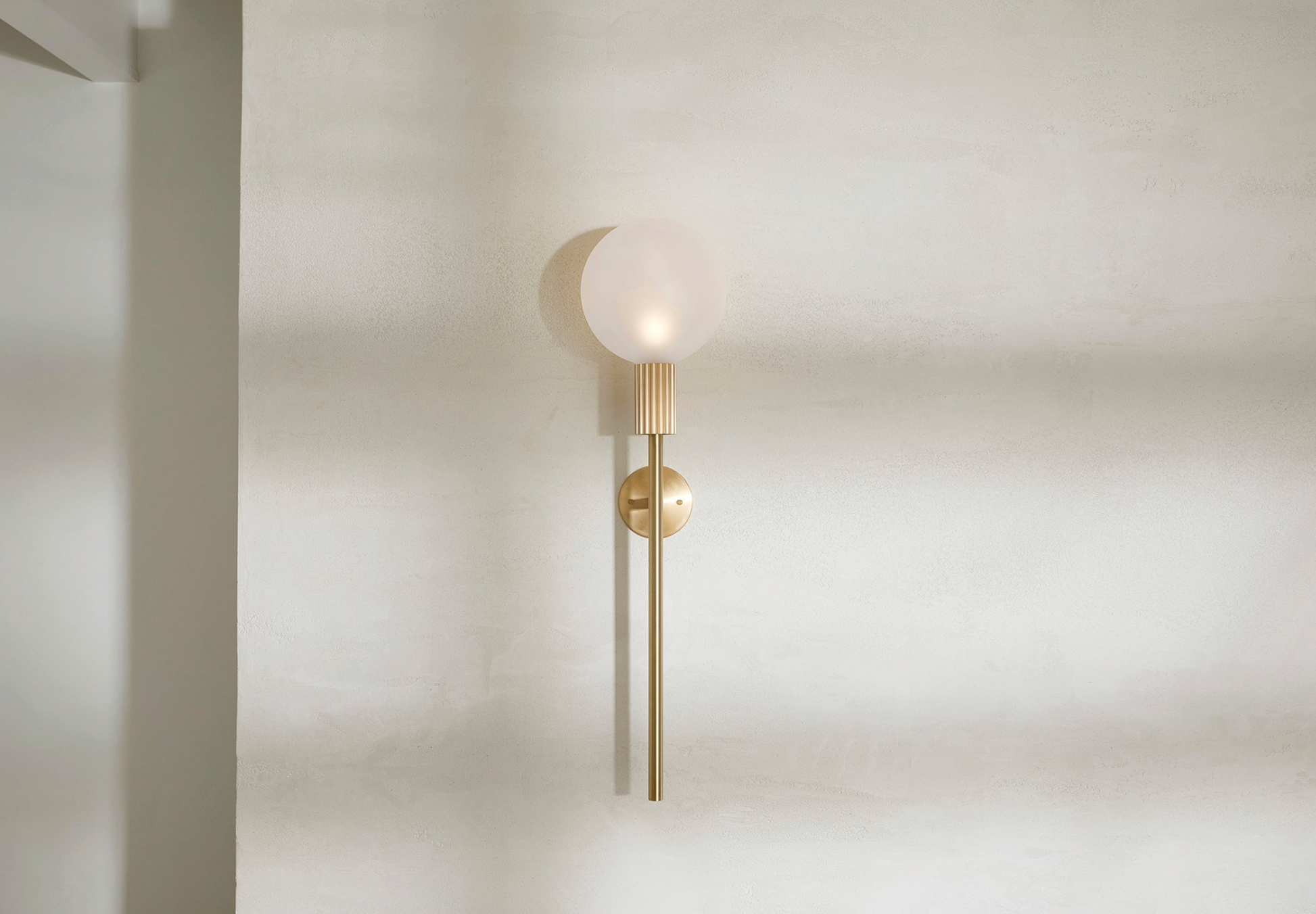Wall-mounted indoor lamp with a spherical bulb and gold fixture on a plain wall.