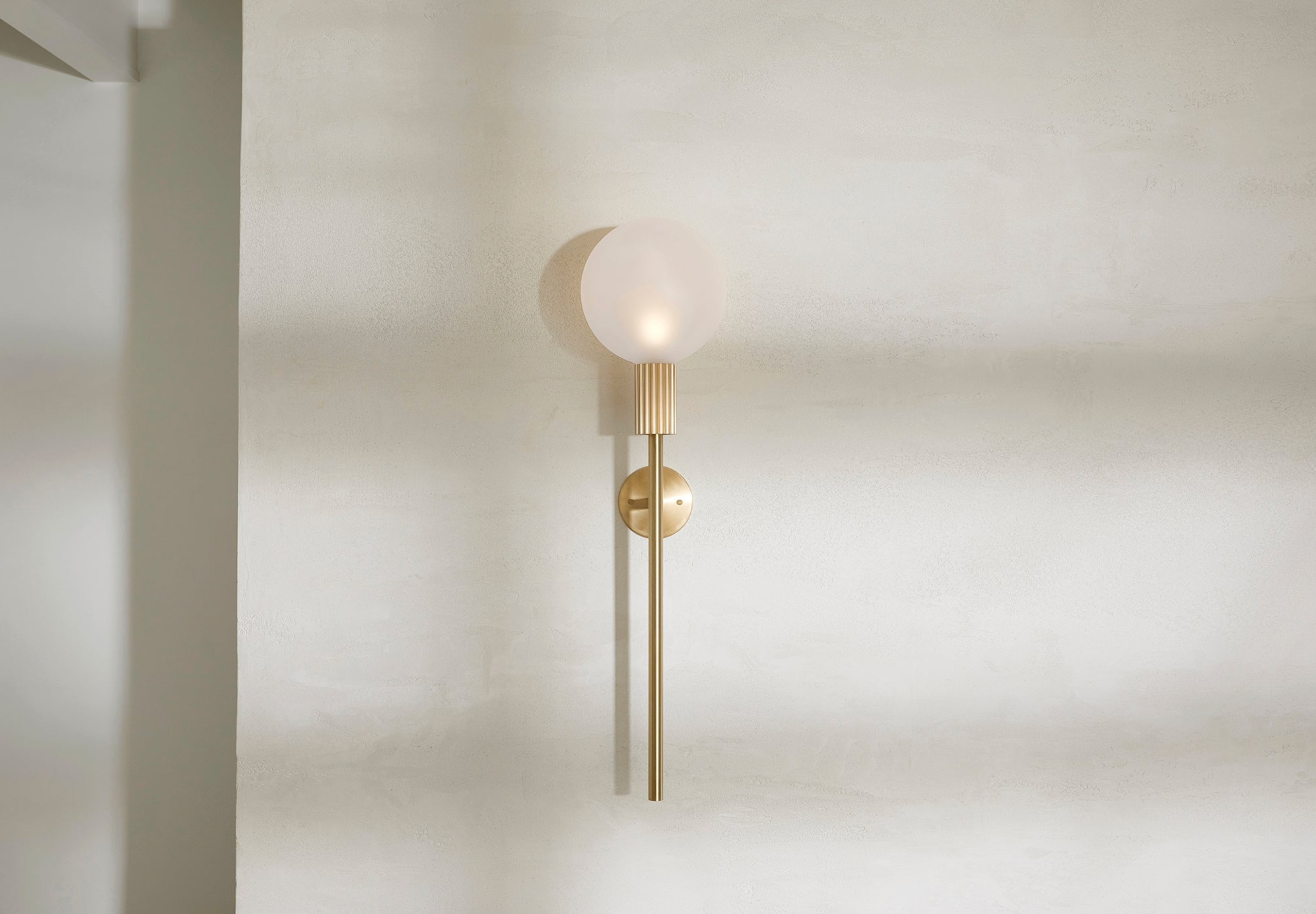 Wall-mounted indoor lamp with a spherical bulb and gold fixture on a plain wall.
