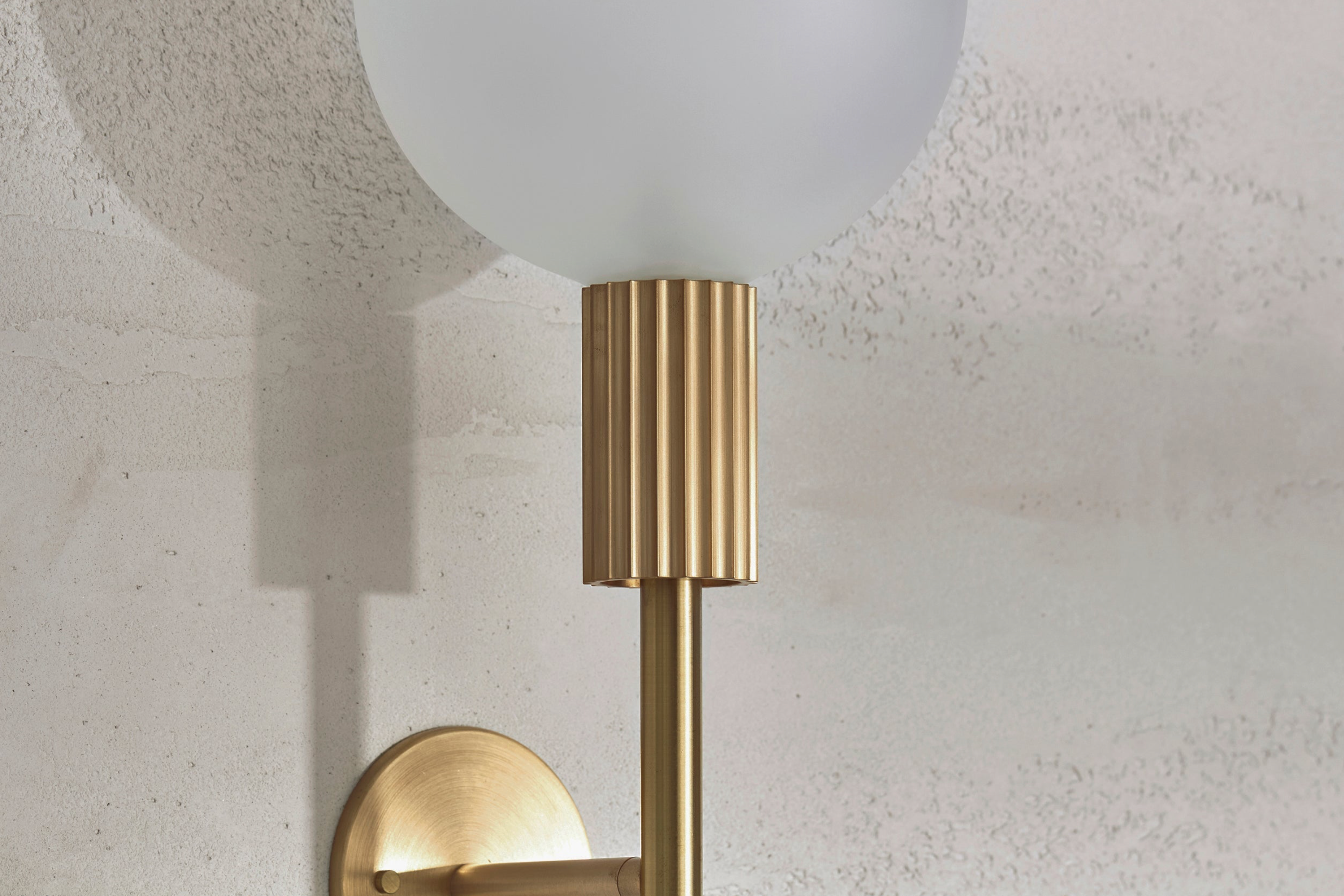 Wall-mounted indoor light fixture with gold finish and white glass shade on a textured wall.